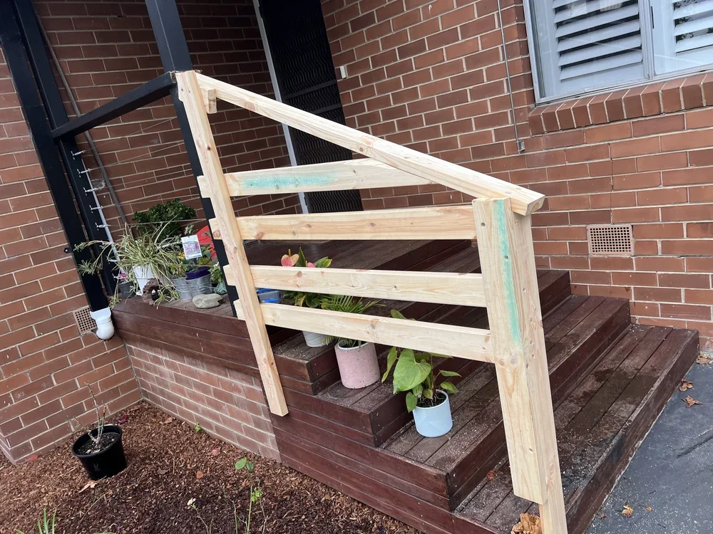 Newly built wooden staircase railing on porch with potted plants.