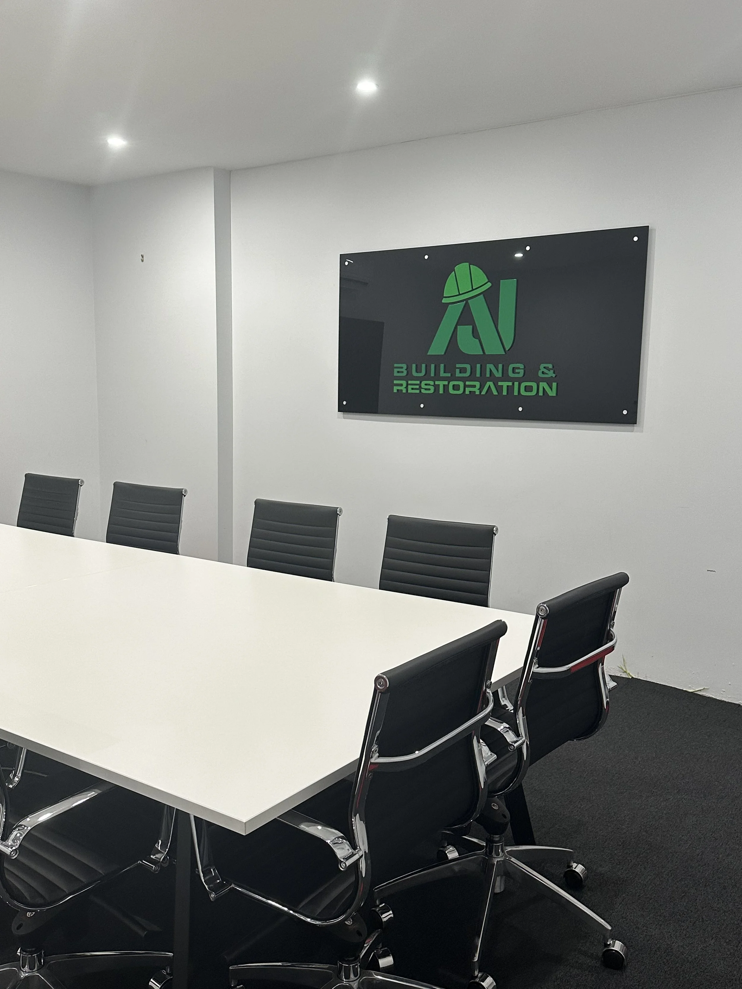 AJ Building & Restoration Board Room With Branded Signage On Wall And White Table And Black Chairs