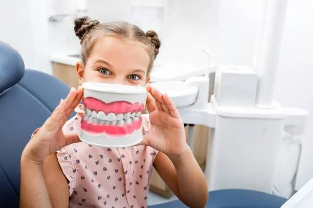 Smiling child holding a large model of teeth while sitting in a dental chair — educational pediatric visit about dental crowns and healthy teeth at Starlight Dental.