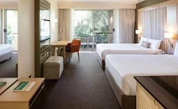 A hotel room with a large bed, a window with curtains, a sitting chair, and a desk.