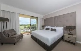 A bedroom with a bed, nightstand, armchair, and a large window showing a view outside.