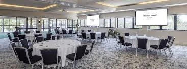 A spacious conference room with round tables covered with white tablecloths and black chairs, large windows, and multiple screens displaying 'MUSEUM'.