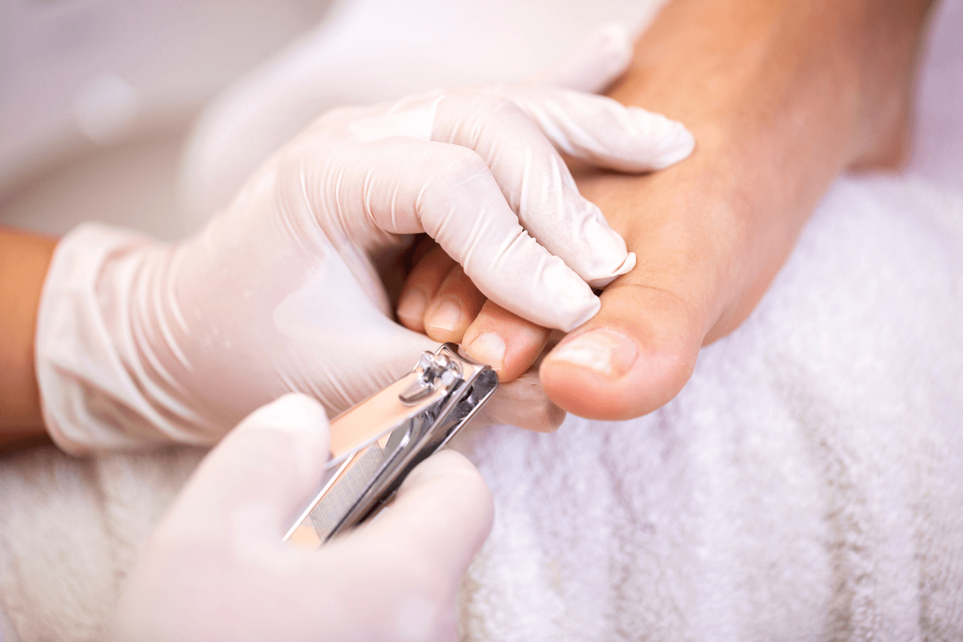 A person receiving a manicure with a close-up of a nail technician filing a client's fingernail using nail clippers, both wearing gloves.