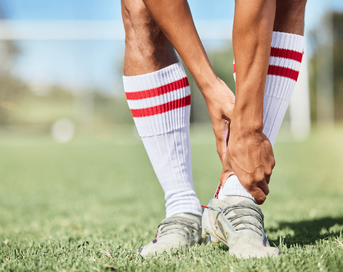 Person wearing white soccer socks with red stripes adjusting their shoe on a grassy field.