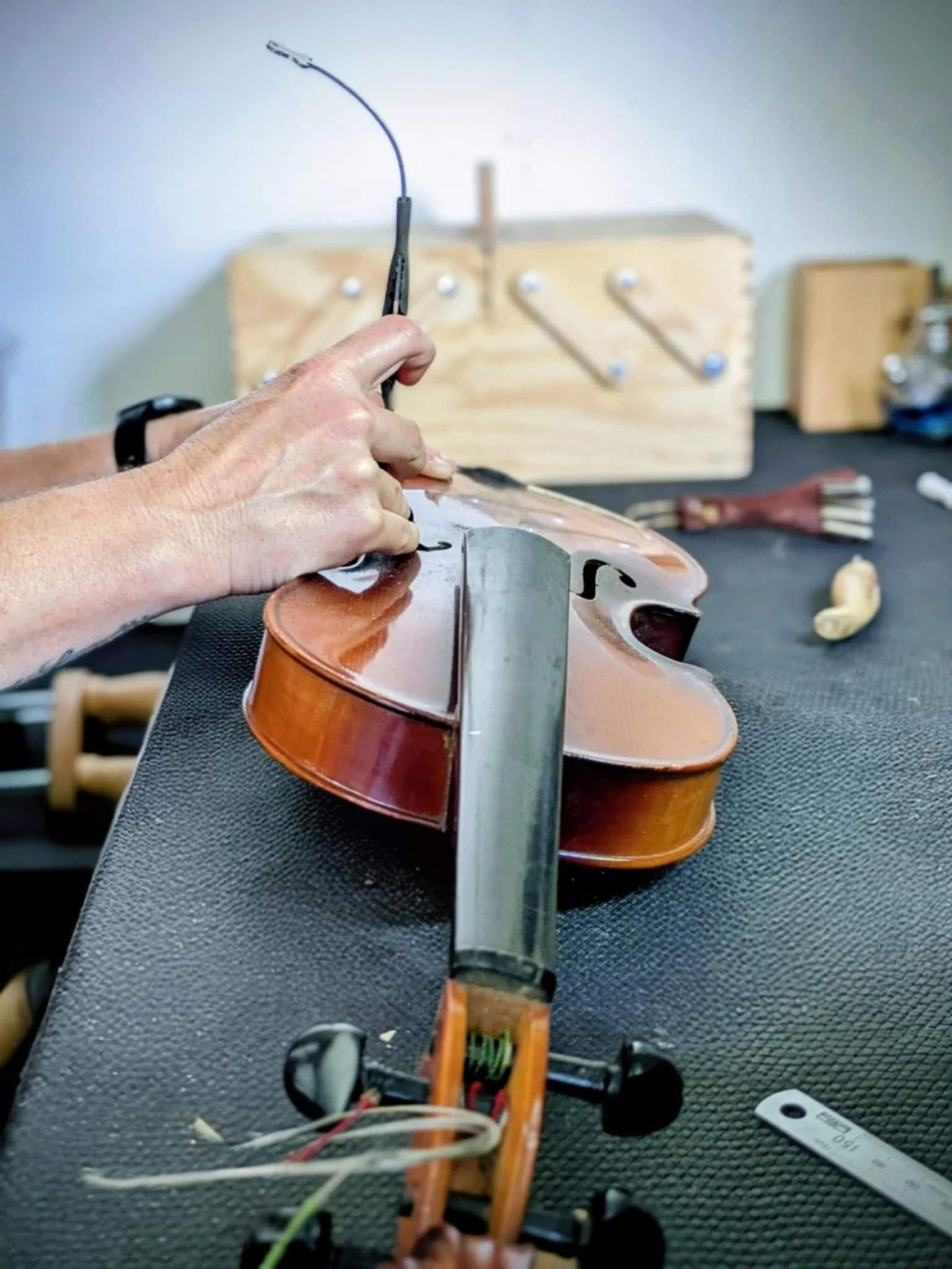 Person repairing a violin on a workbench, with tools and a wooden work box in the background.