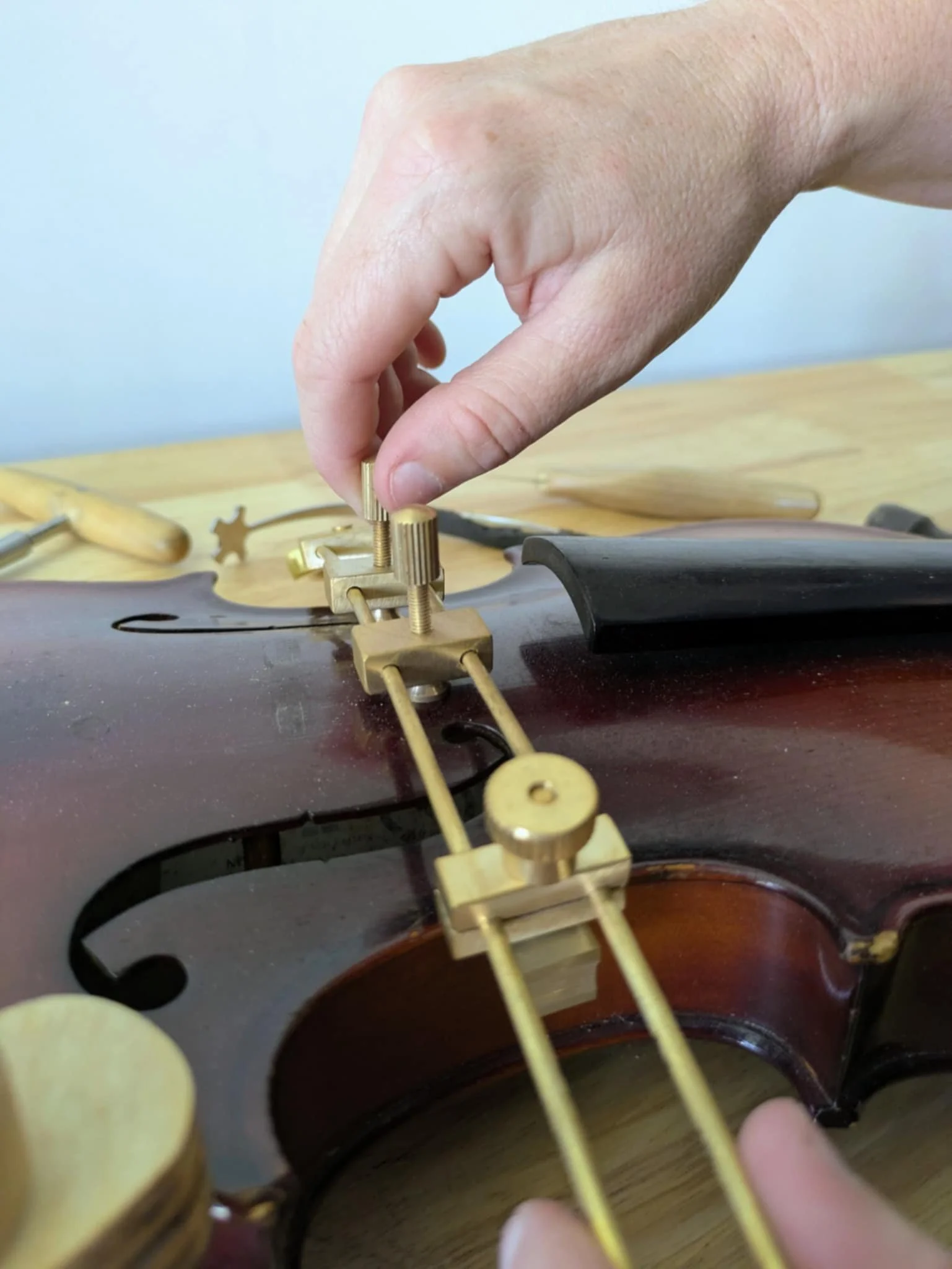 Close-up of a person's hand adjusting the bridge of a vintage violin with tools on a wooden workbench.