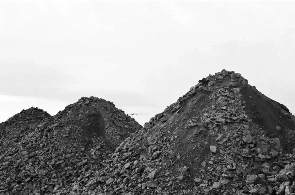 Three large piles of dark, loose rocks or dirt outdoors under a cloudy sky.