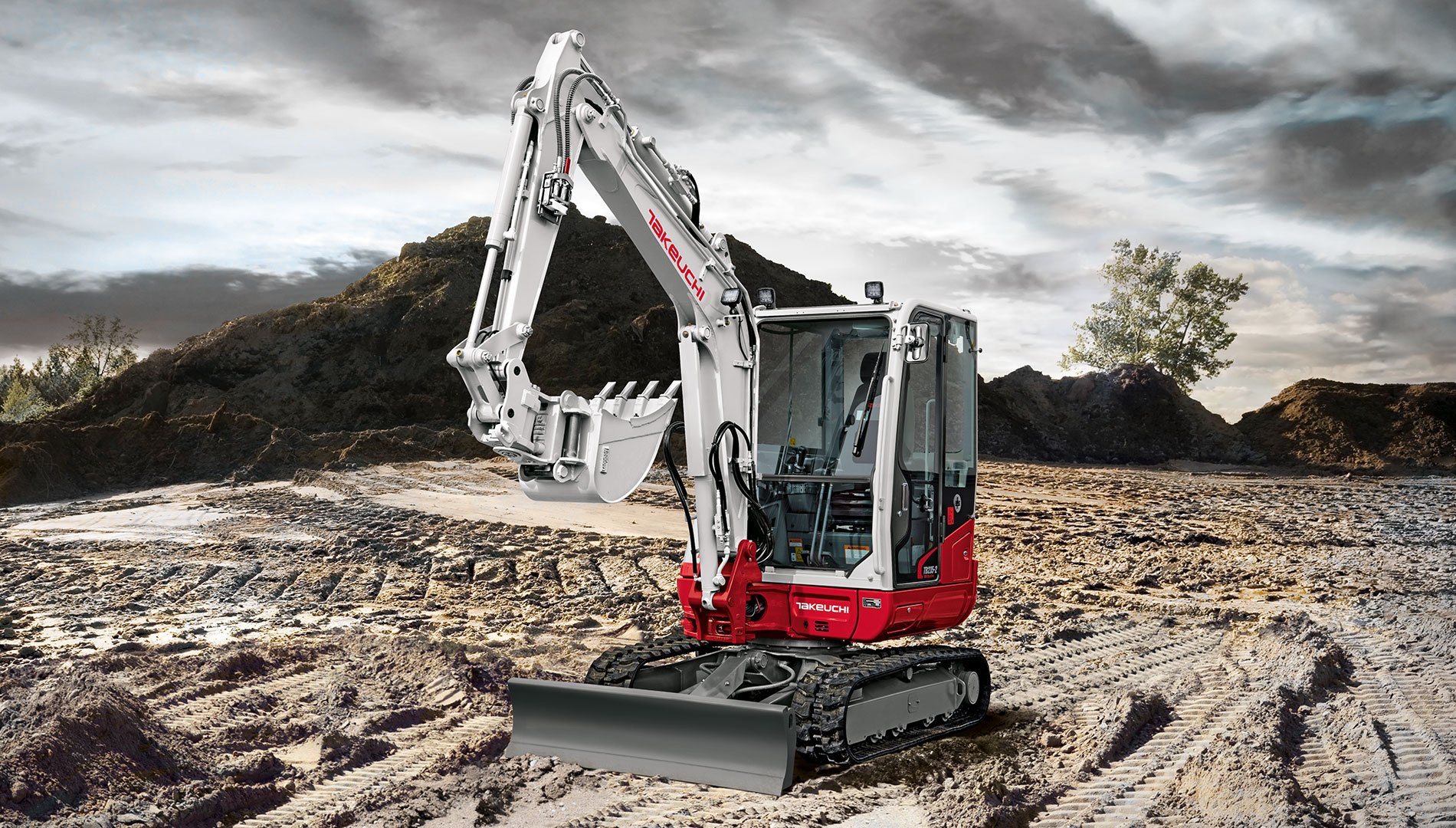 A white and red mini excavator on a construction site with dirt and mountains in the background.