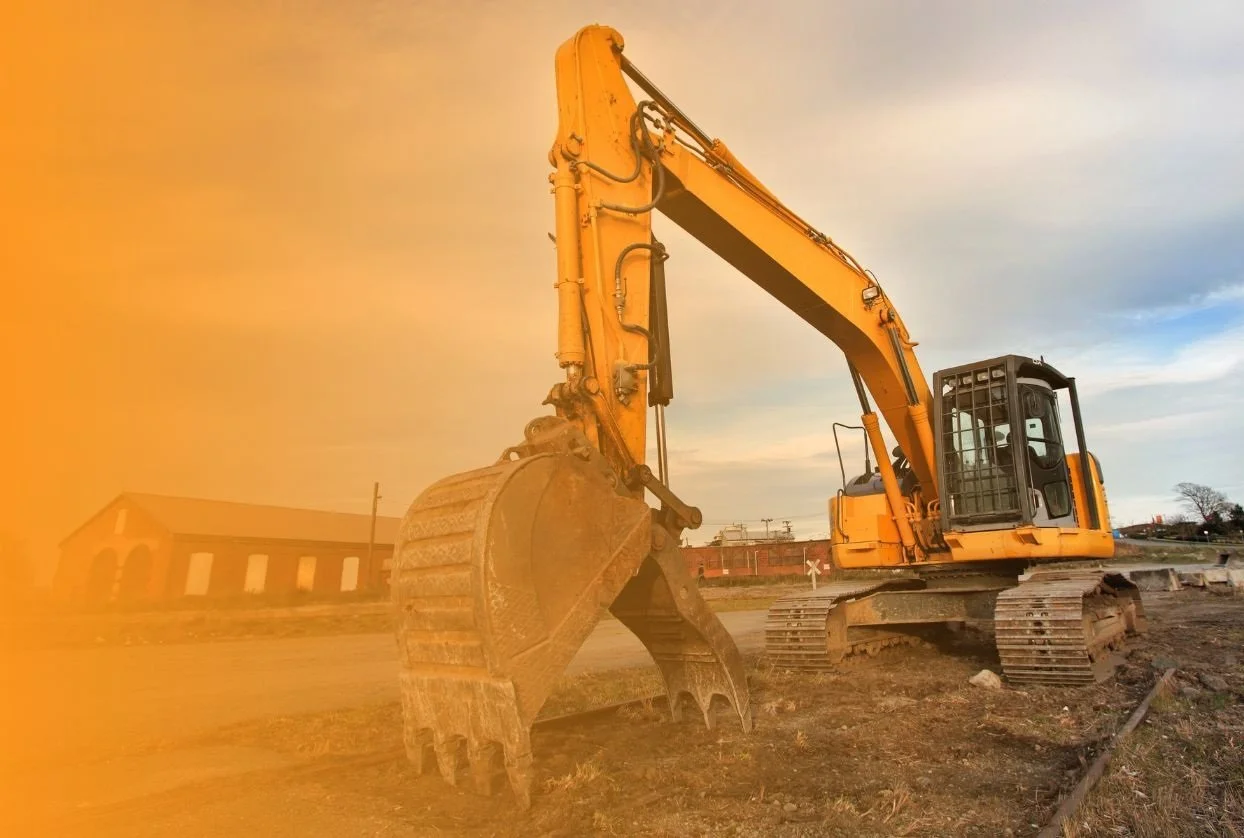 Yellow excavator at a construction site during sunset with a building in the background.