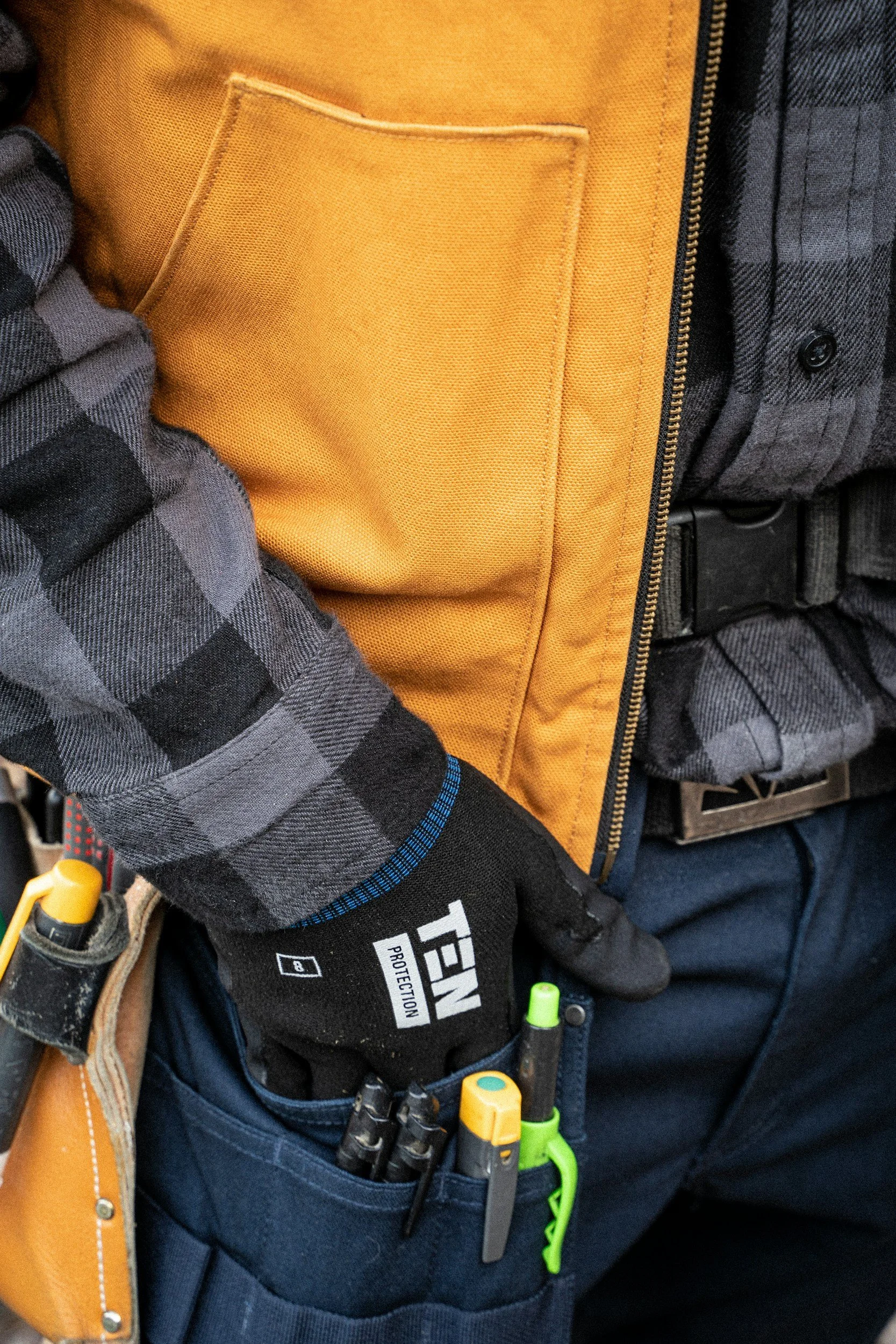 Close-up of a worker wearing a flannel shirt, gloves, and a tool belt filled with tools.