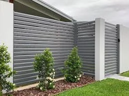 Modern grey horizontal-slat fence Brisbane with white posts, bordered by neatly landscaped shrubs and lawn.