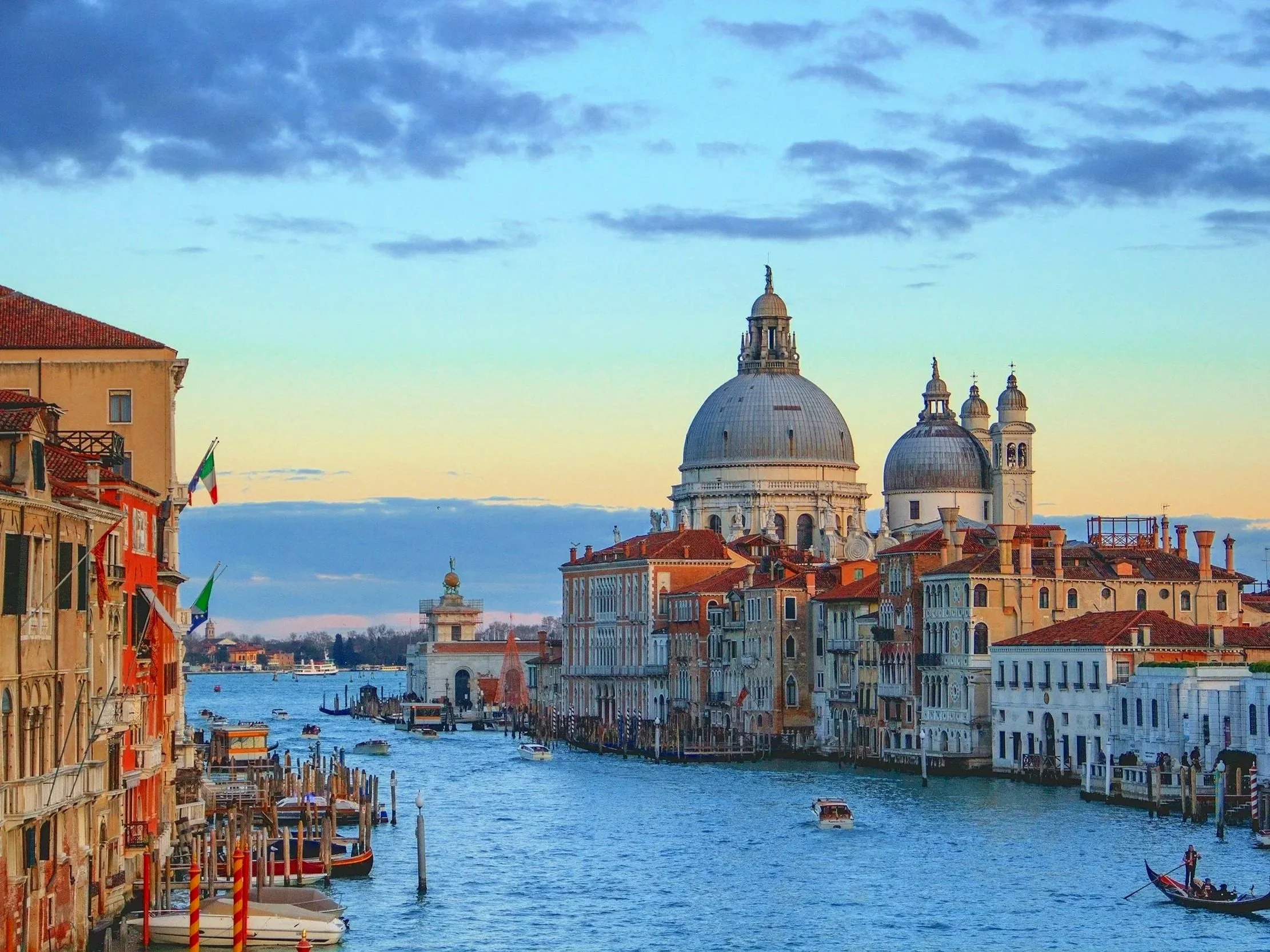 Vista del canal de Venecia con edificios históricos, gondolas y un cielo con nubes al atardecer.