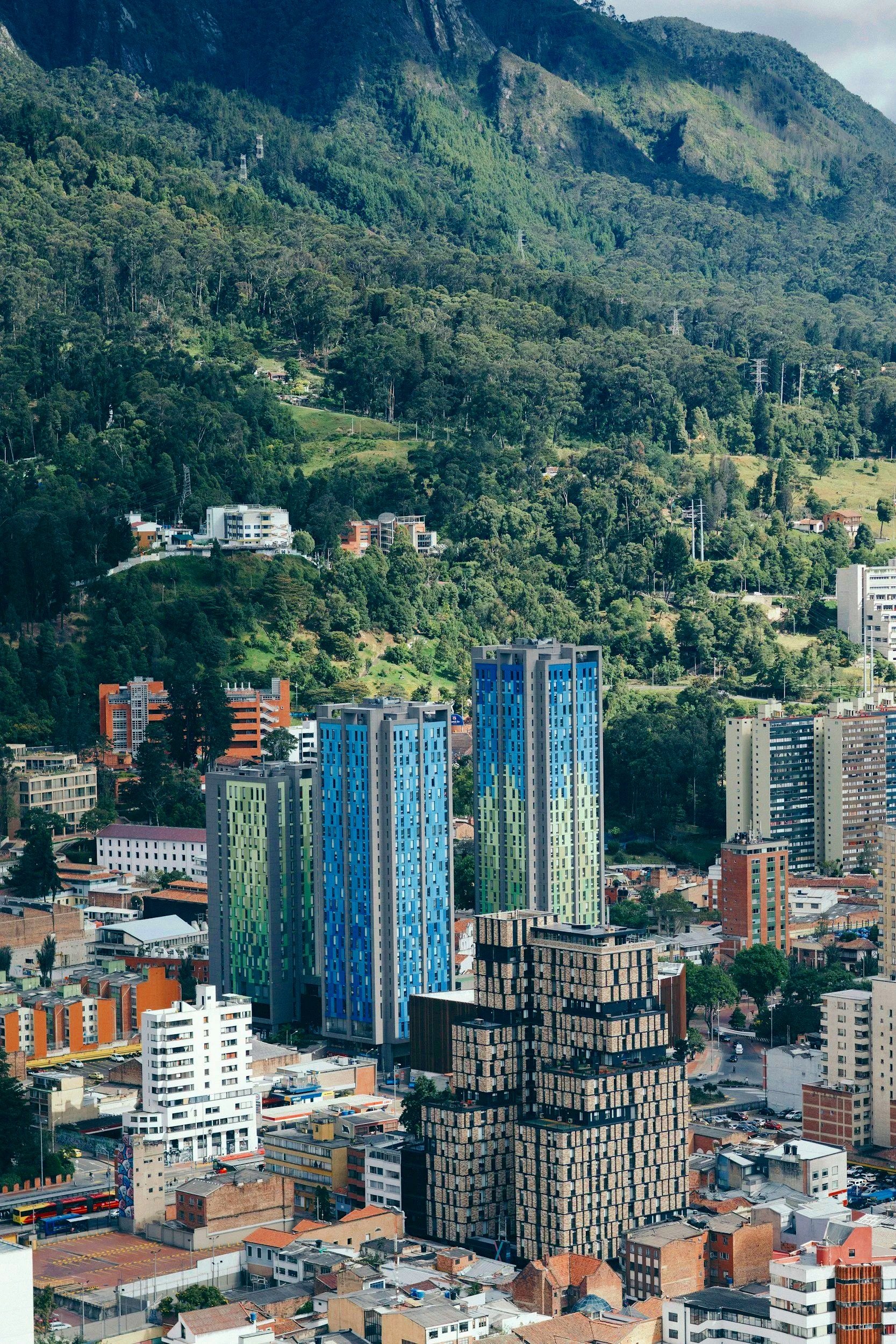 Cityscape with colorful high-rise buildings in front and green forested hills in the background.