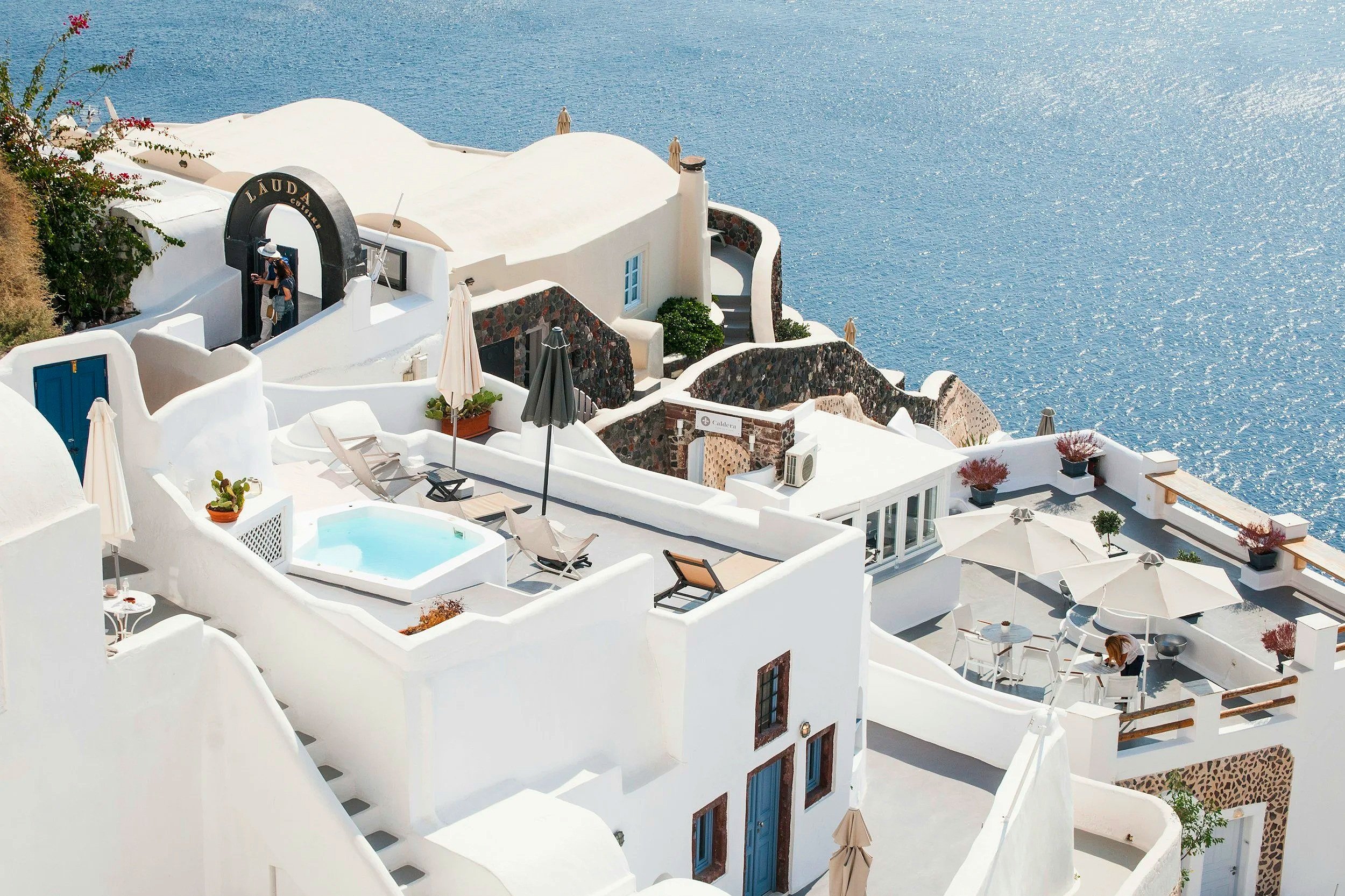 Vista aérea de casas blancas con terraza y jacuzzi junto al mar en Santorini, Grecia.