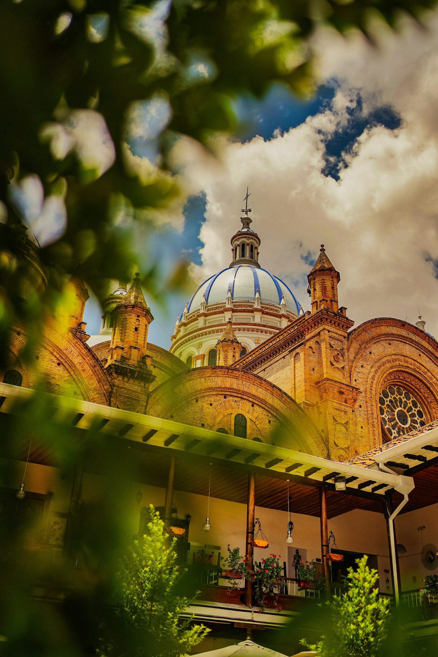 Vista de una catedral con cúpula azul y techo de tejas, vista desde un patio con plantas y toldo.