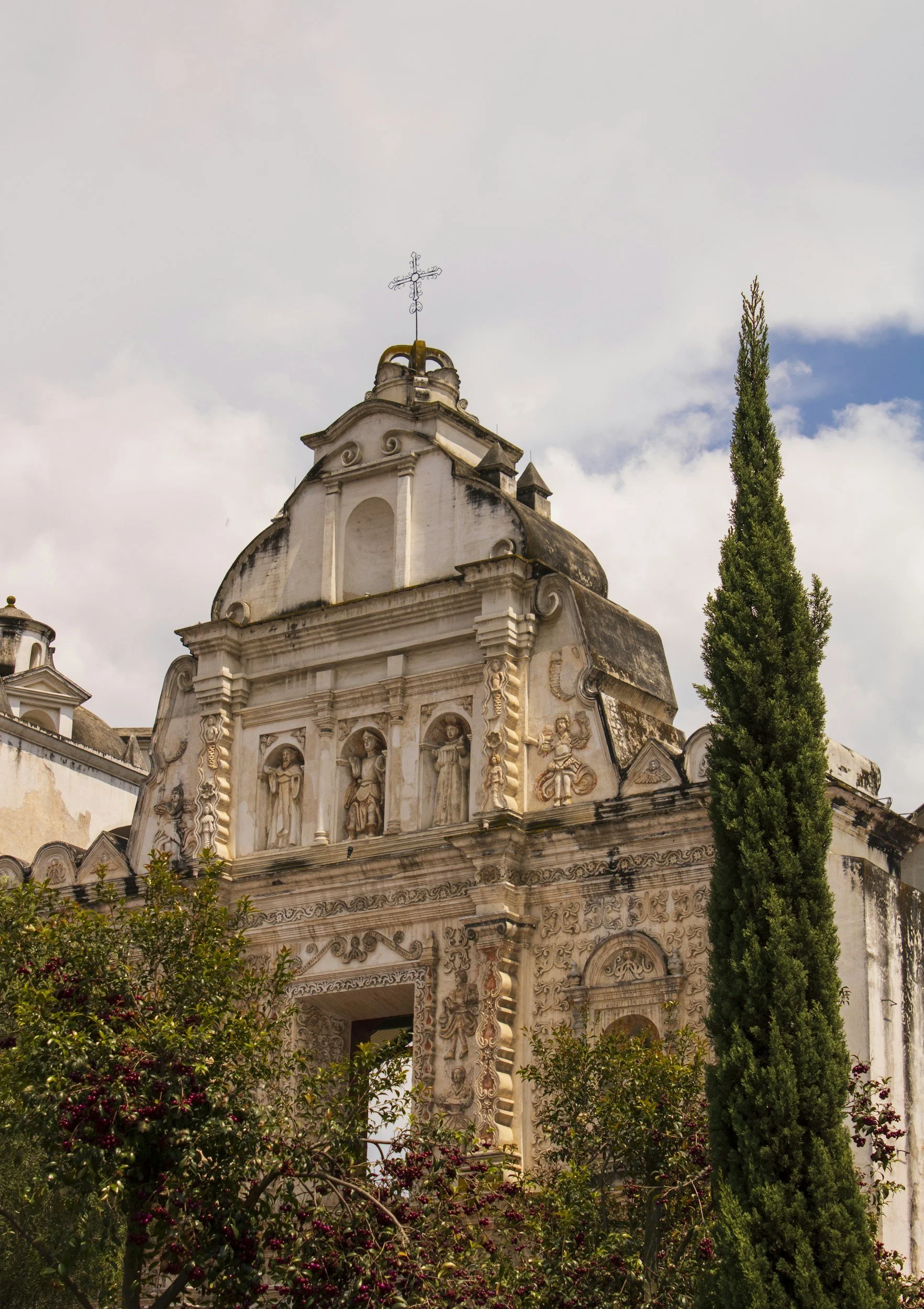 Fachada de una iglesia colonial con esculturas y detalles ornamentales, rodeada de árboles.