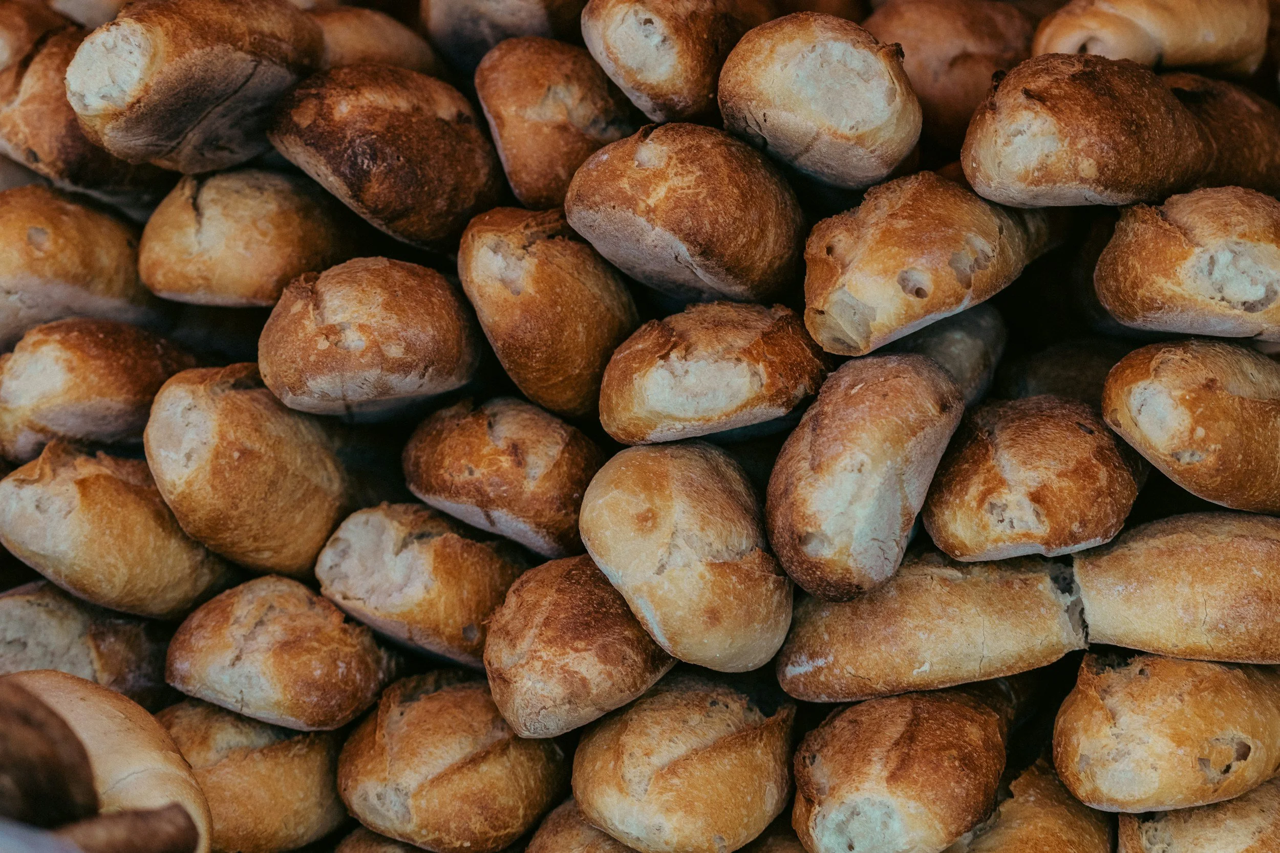 Heap of small, freshly baked bread rolls with a golden-brown crust.