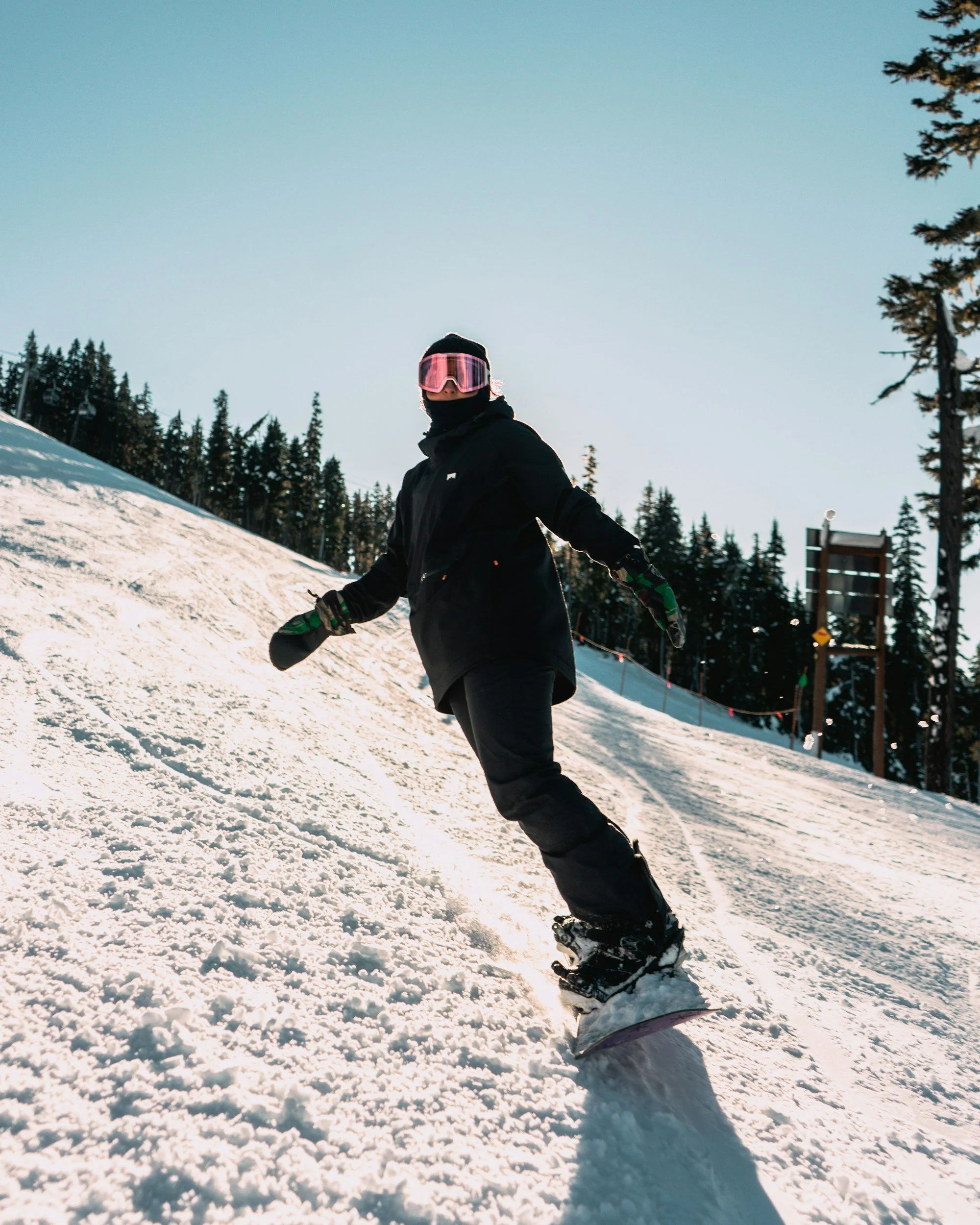 Person snowboarding on a snowy slope with pine trees in the background.
