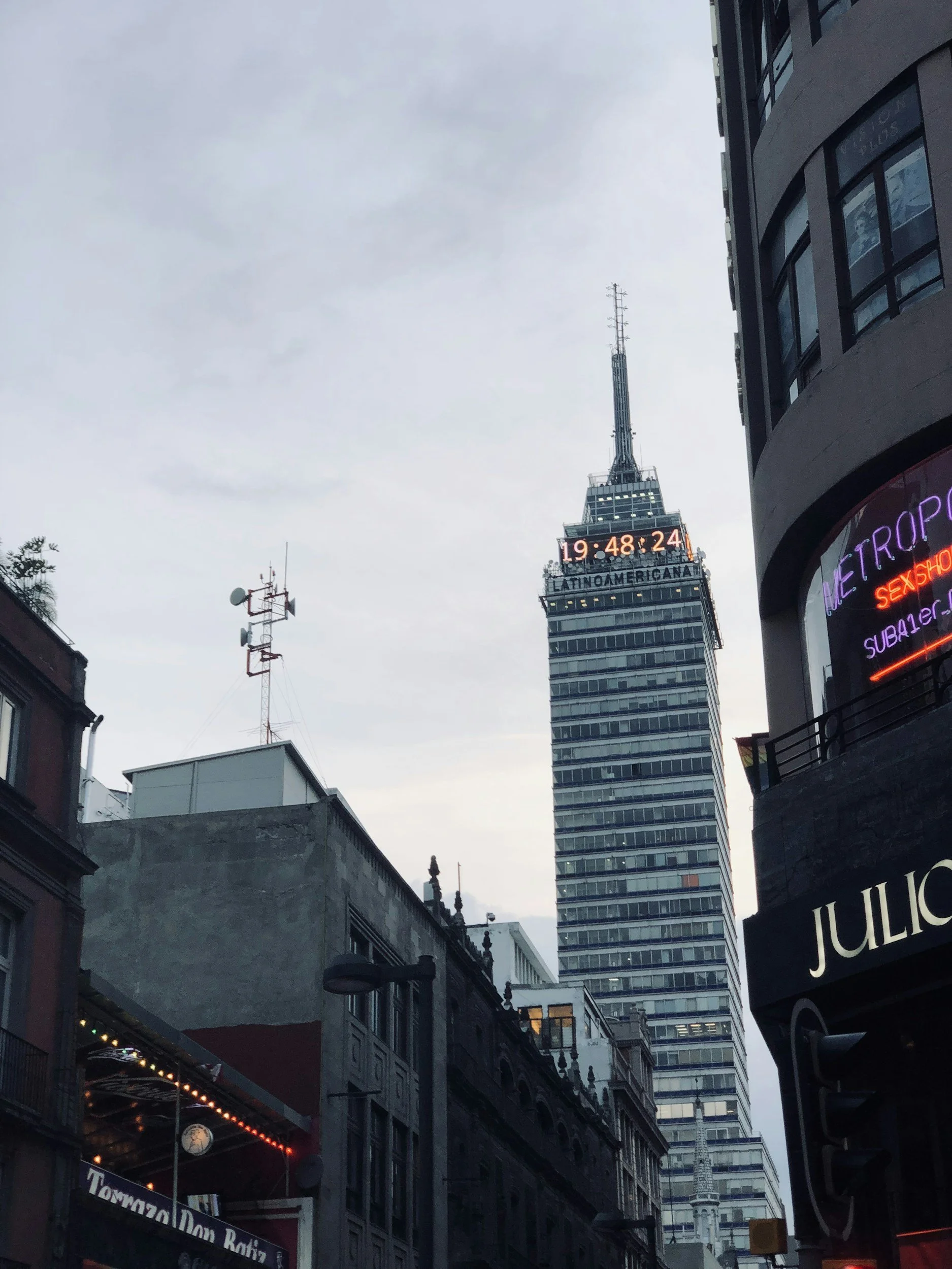 Cityscape with tall skyscraper, digital clock, and surrounding buildings.