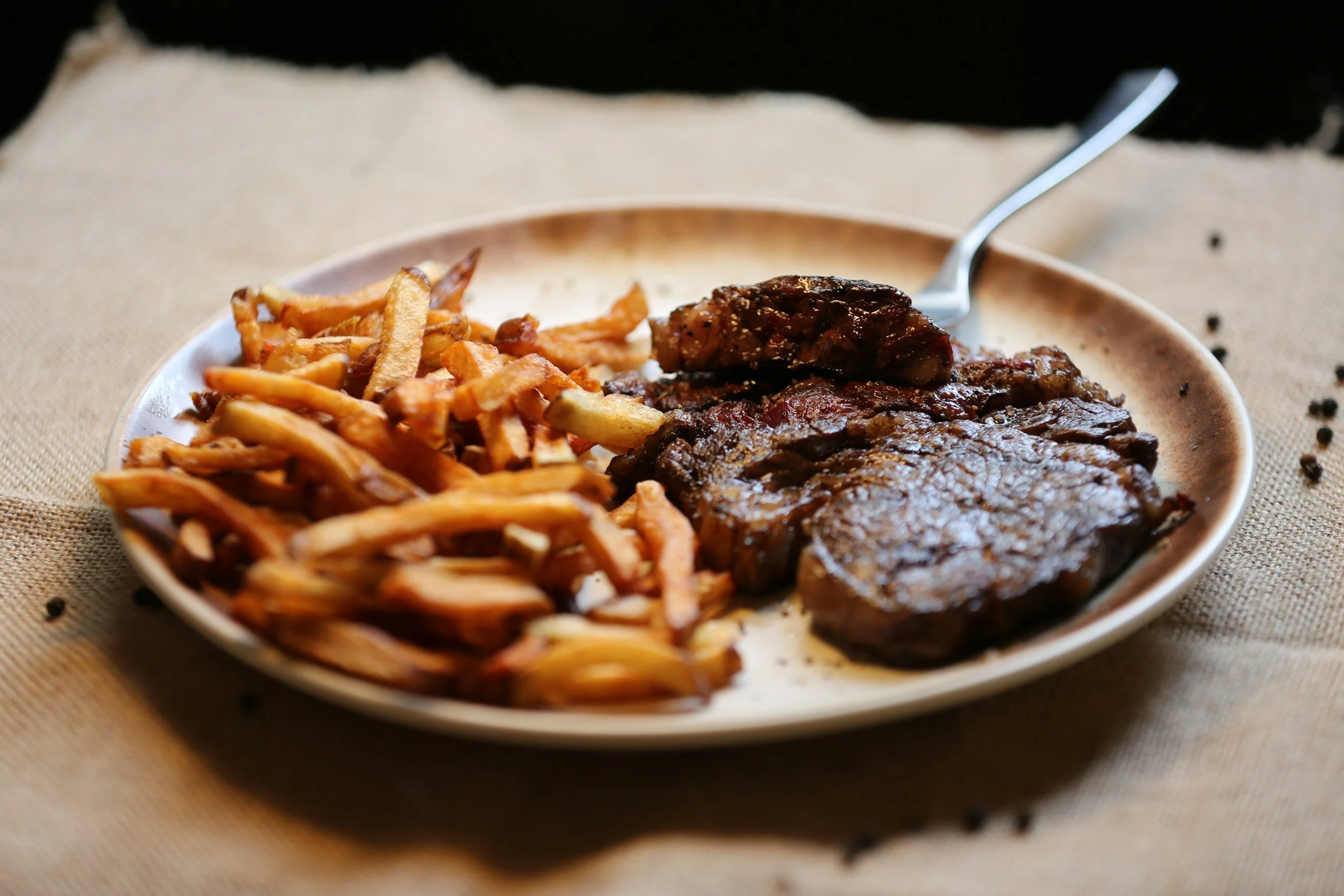 Plate with French fries, grilled beef steak, and a piece of cooked meat on a beige plate.