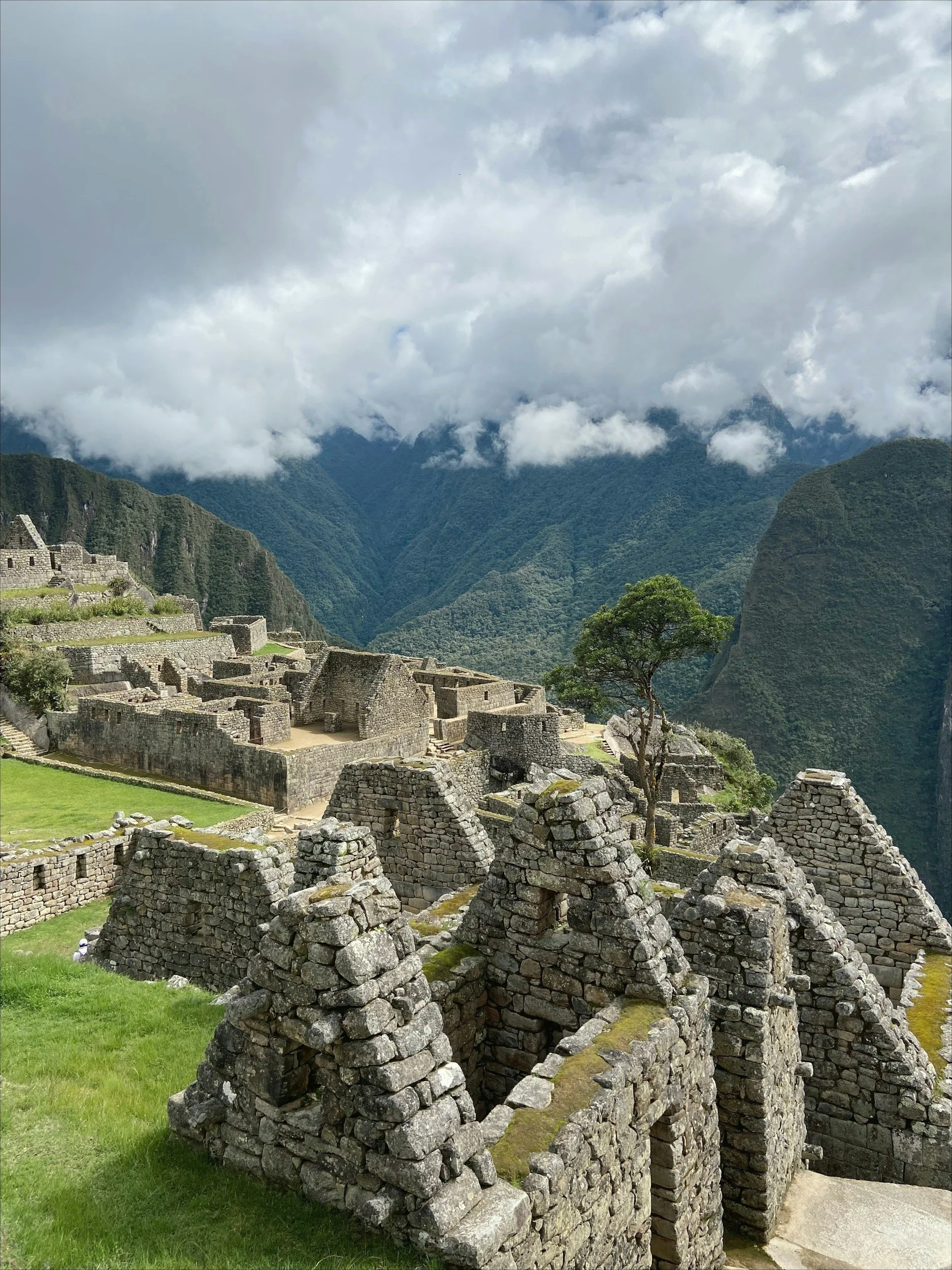 Ancient stone ruins at Machu Picchu in Peru, surrounded by green mountains and cloudy sky.