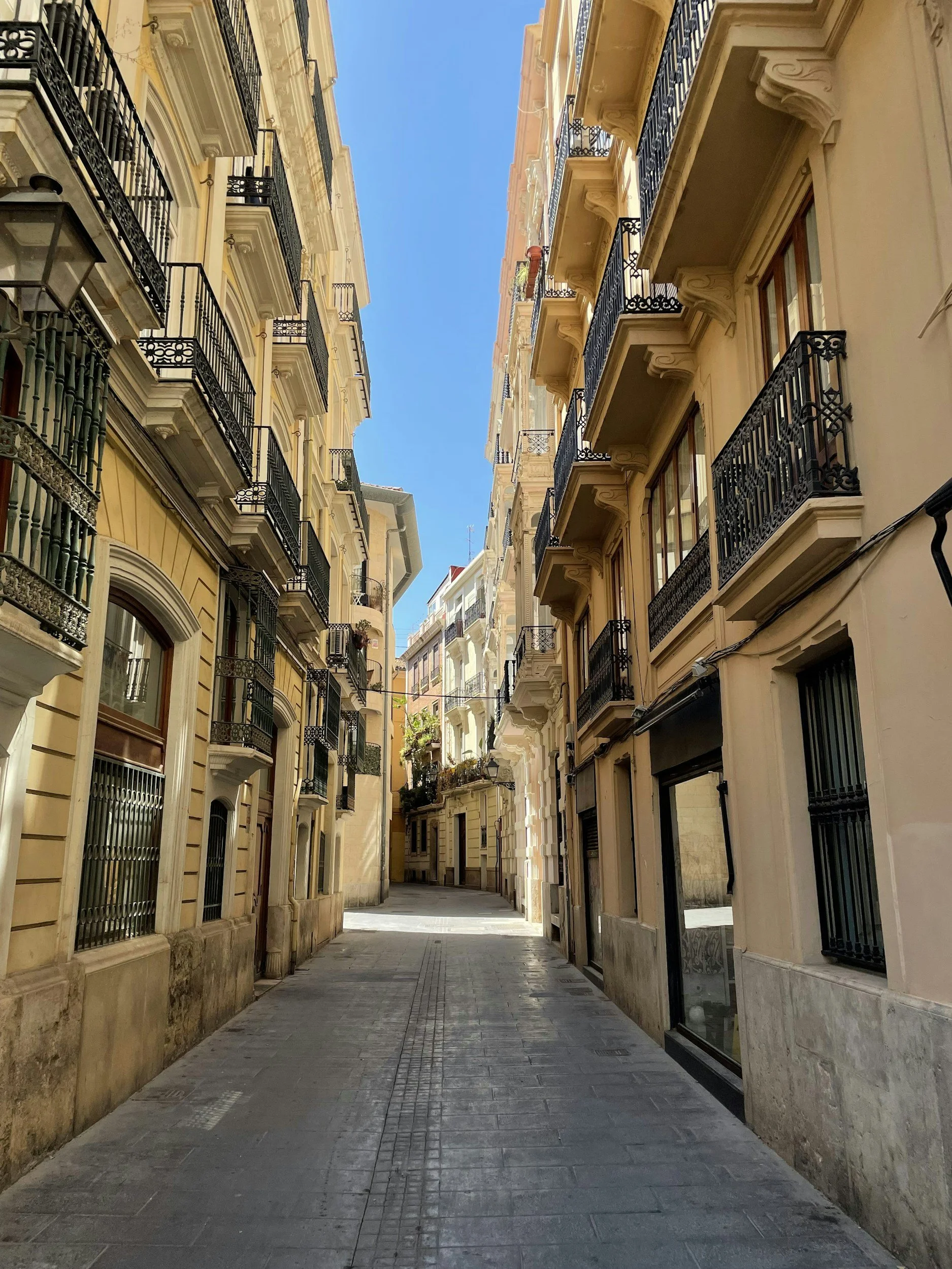A narrow street lined with tall, colorful apartment buildings with balconies against a bright blue sky.