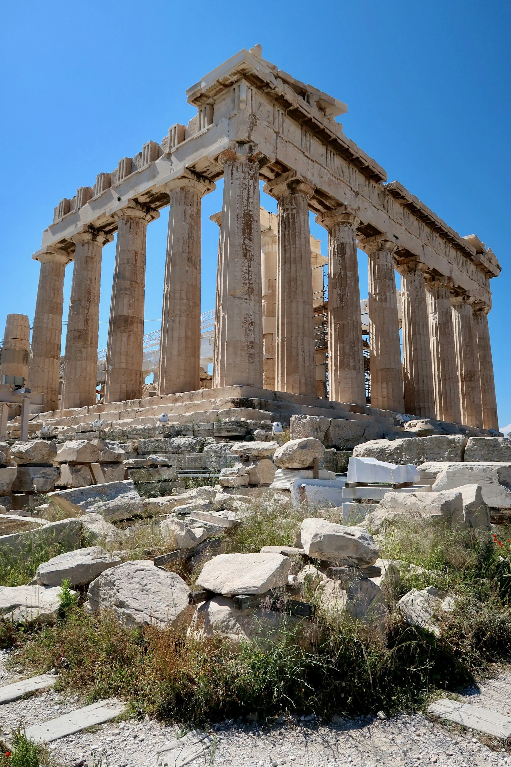 Ruinas antiguas del Partenón en Grecia, con columnas y pedazos de piedra en el suelo, bajo un cielo azul.