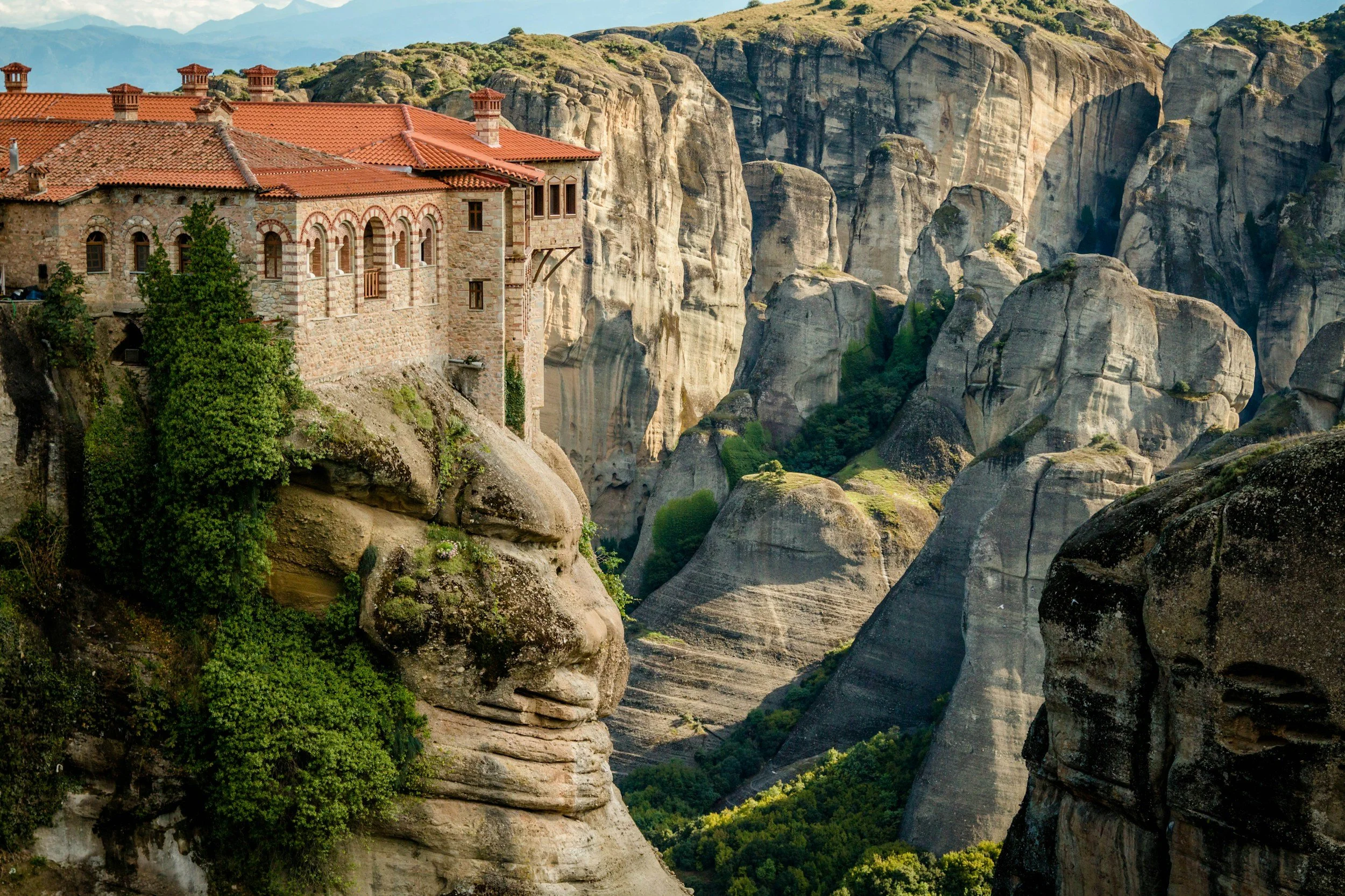 Un monasterio construido en un acantilado rocoso, rodeado de formaciones rocosas y vegetación, en un entorno montañoso.