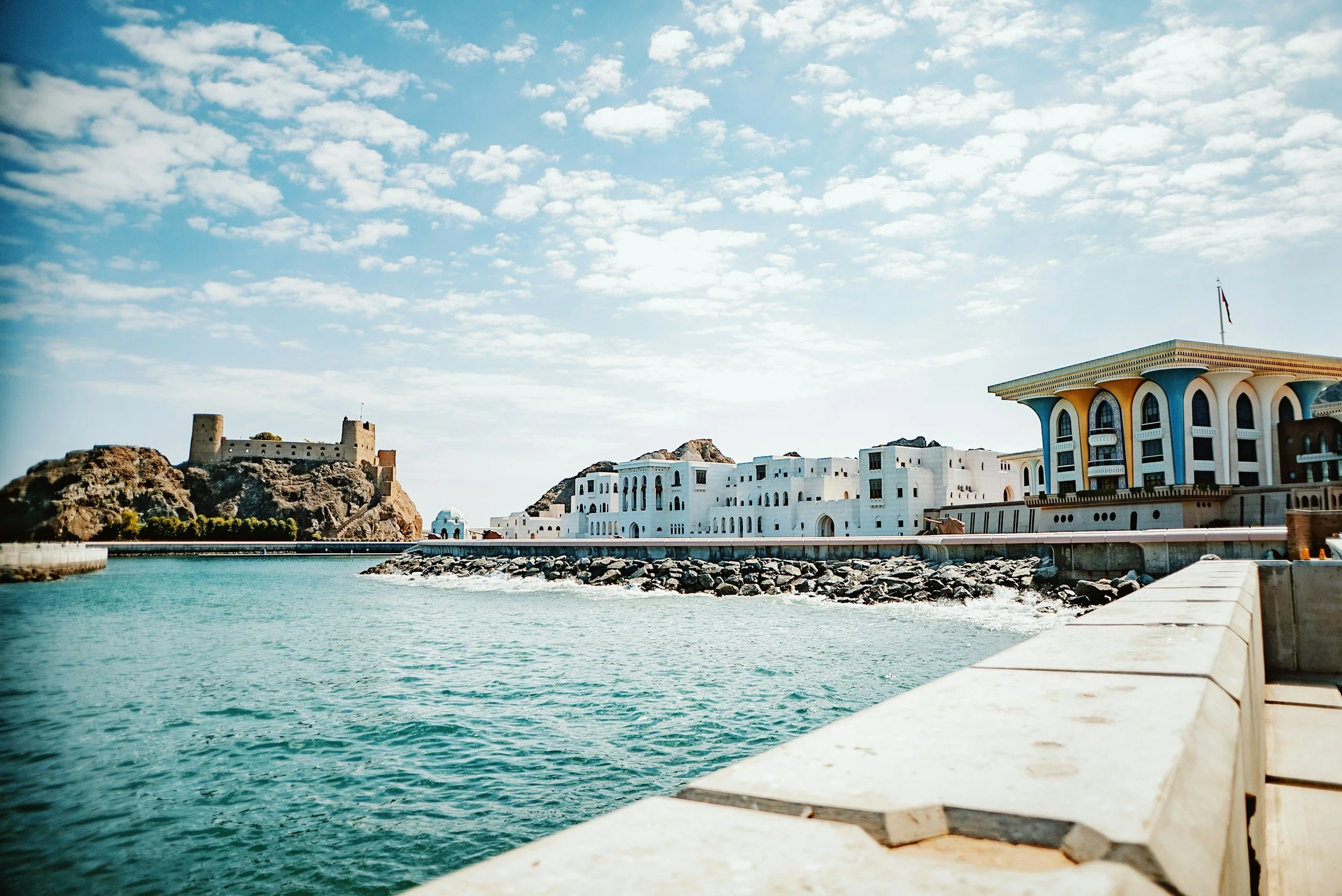 Paisaje costero con edificios blancos, un castillo en una colina y un mar azul