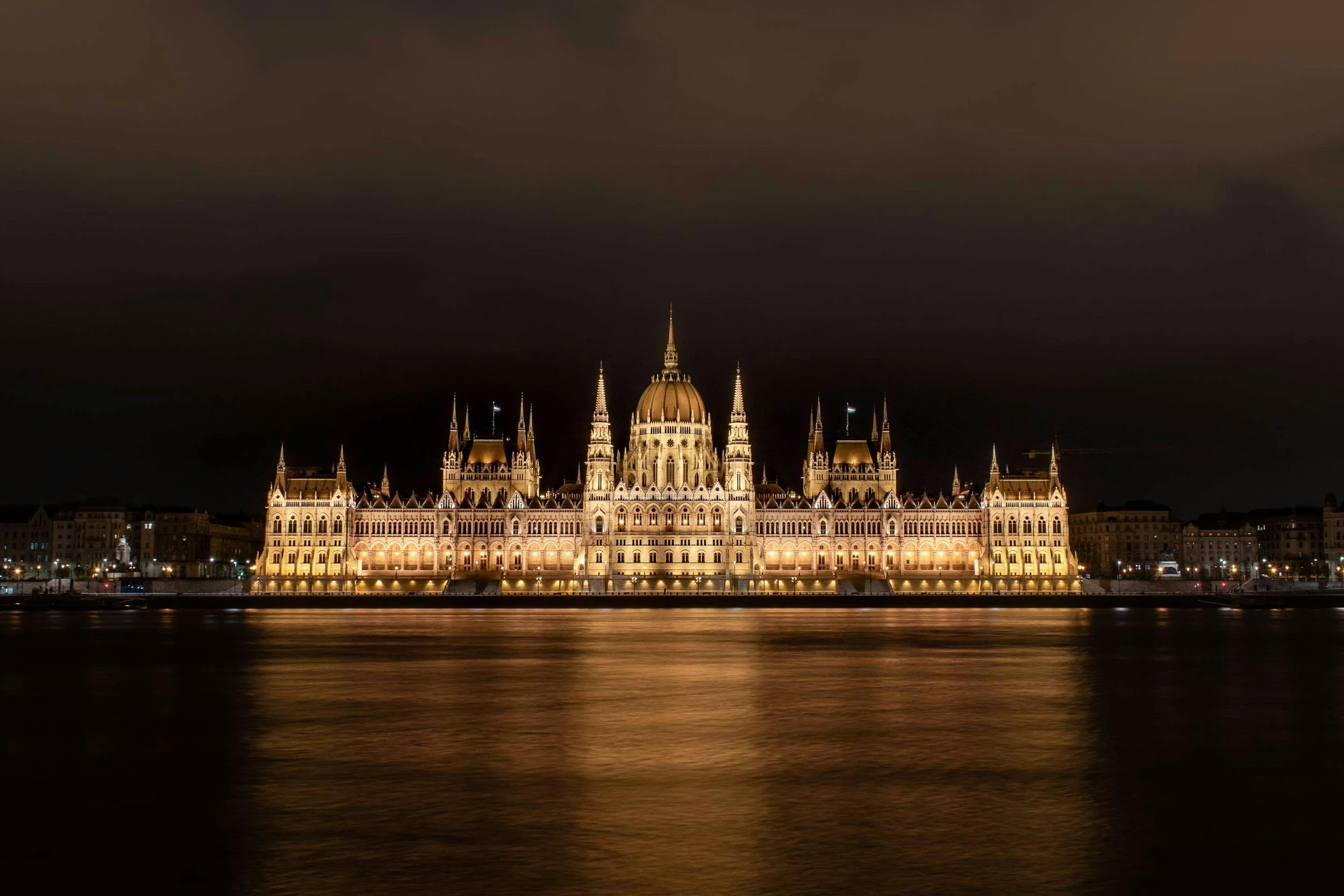 Vista del Parlamento de Budapest iluminado por la noche frente al río con reflejos en el agua.