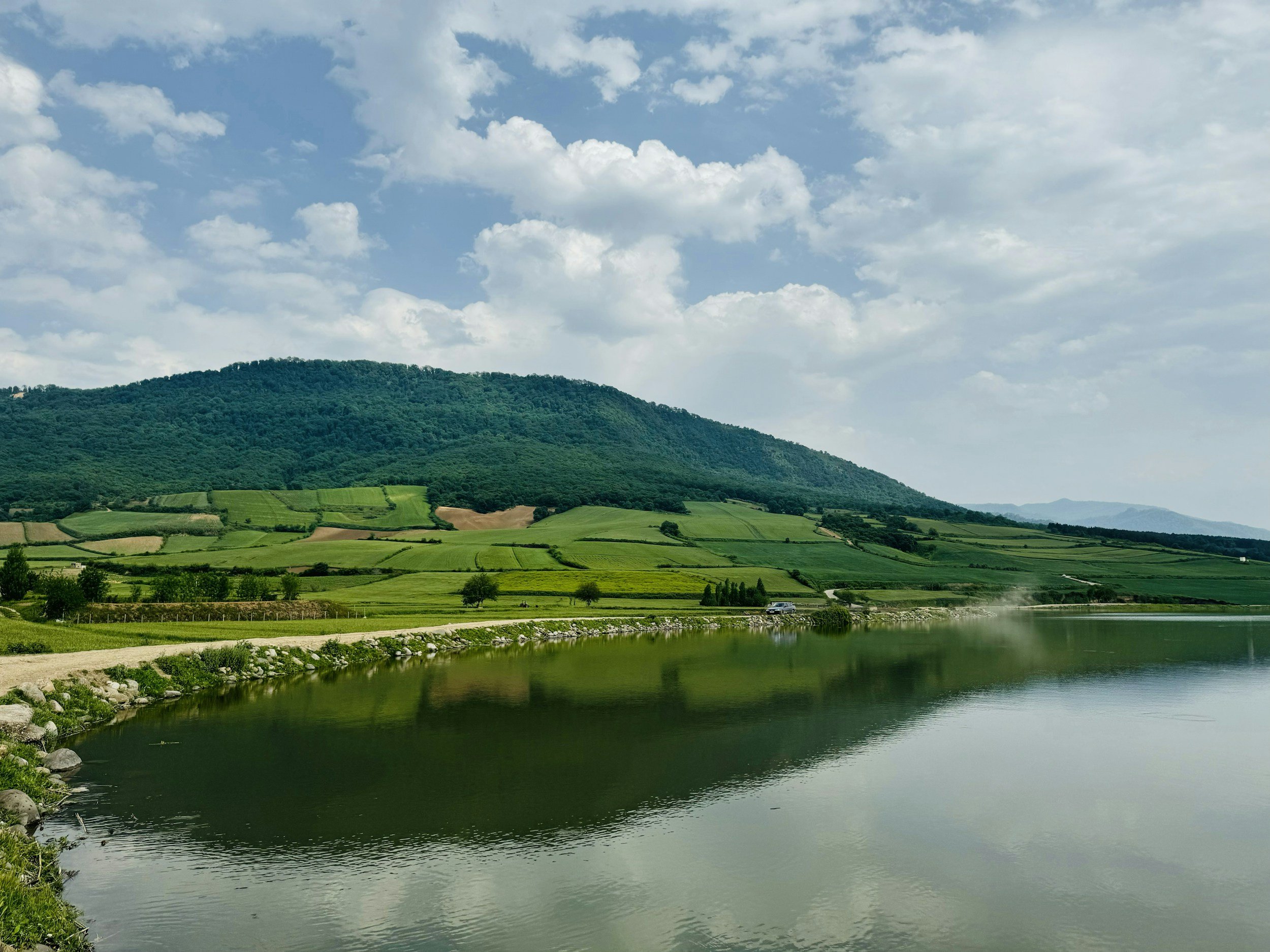 Paisaje con colinas verdes, río y cielo con nubes, en un día soleado.