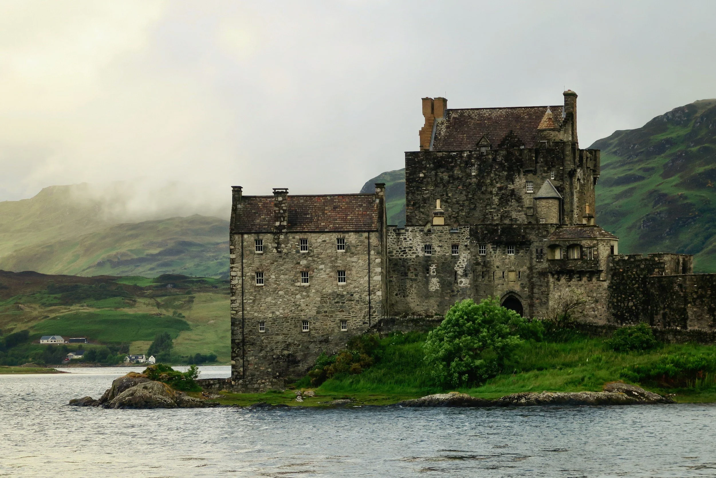 Castillo antiguo de piedra en una isla rodeada por agua y colinas verdes con niebla en el fondo