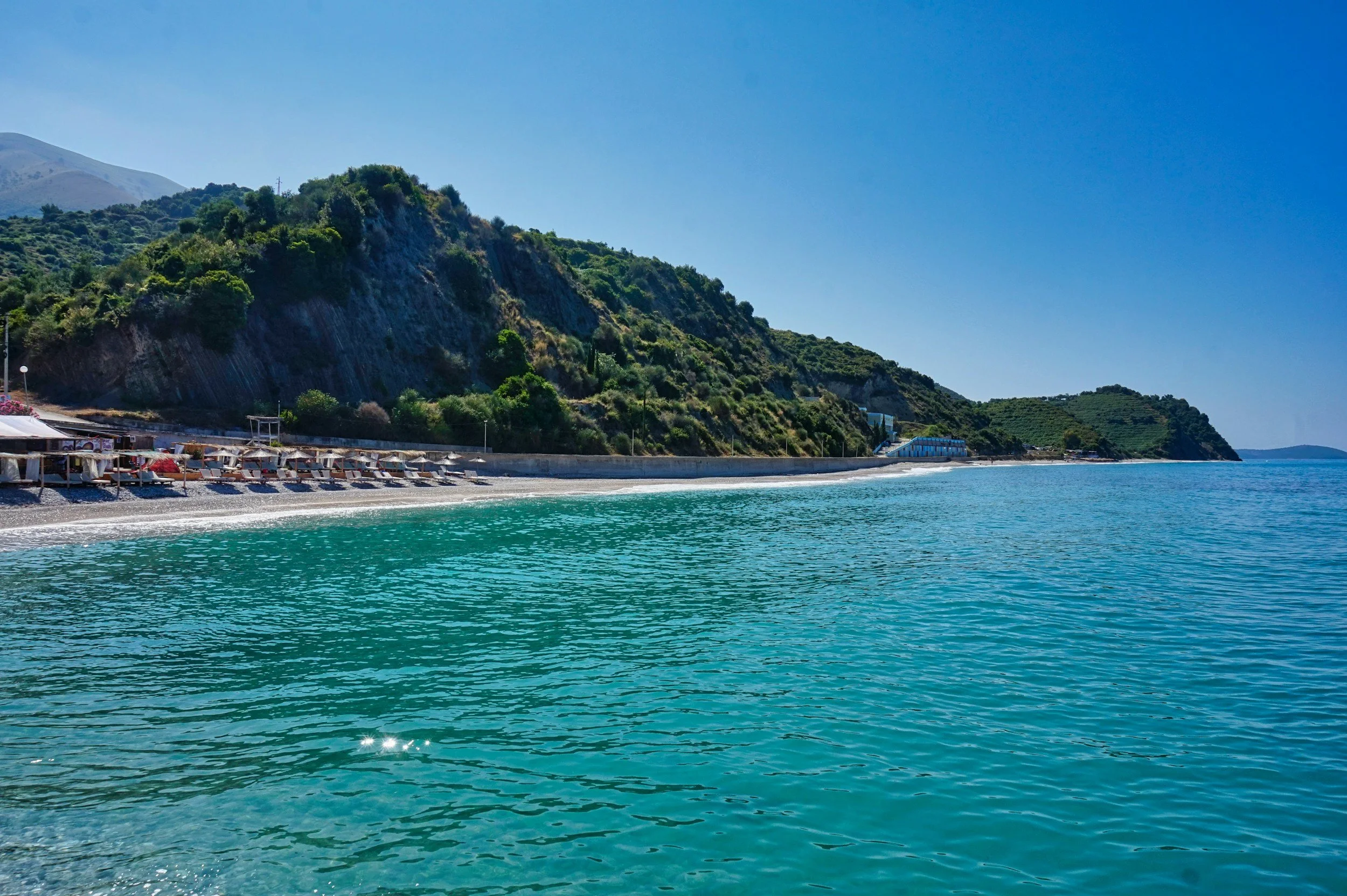 Playa con sombrillas y tumbonas junto a un paisaje montañoso y mar azul