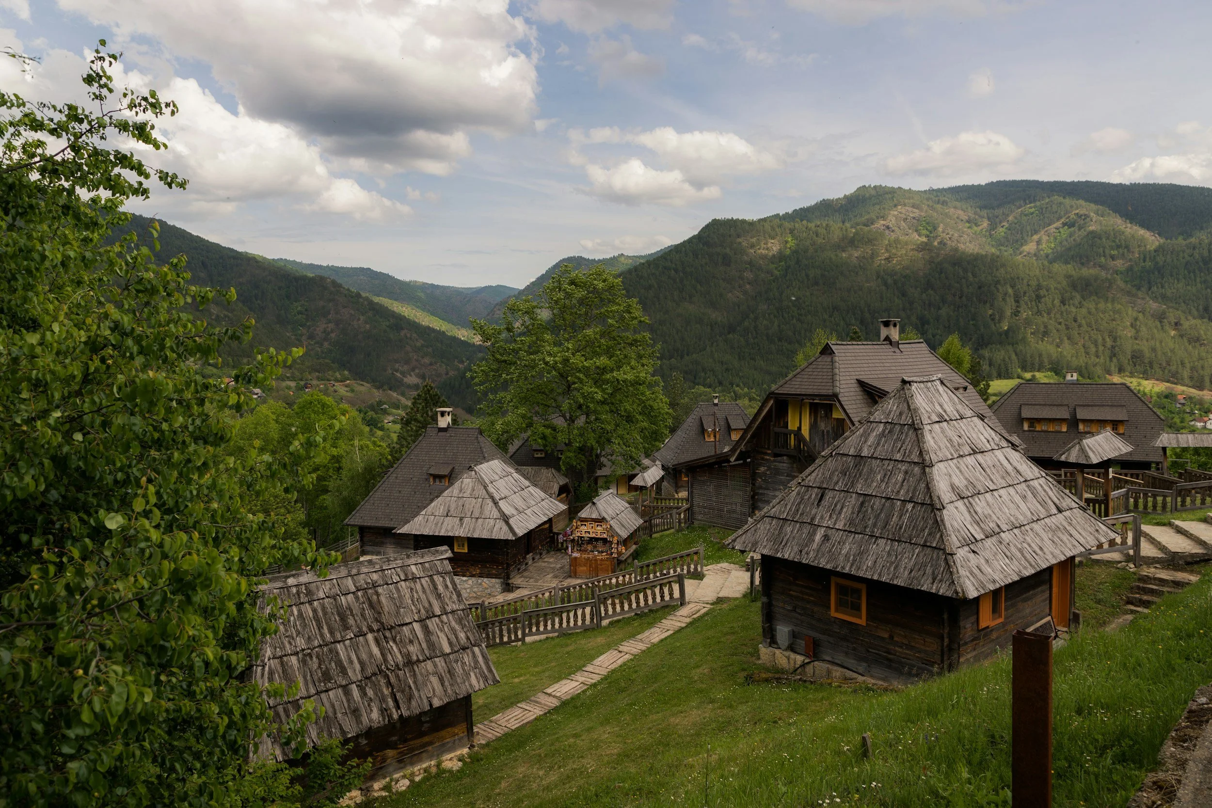 Casas de madera tradicionales en una colina rodeadas de árboles y montañas verdes bajo un cielo con nubes.