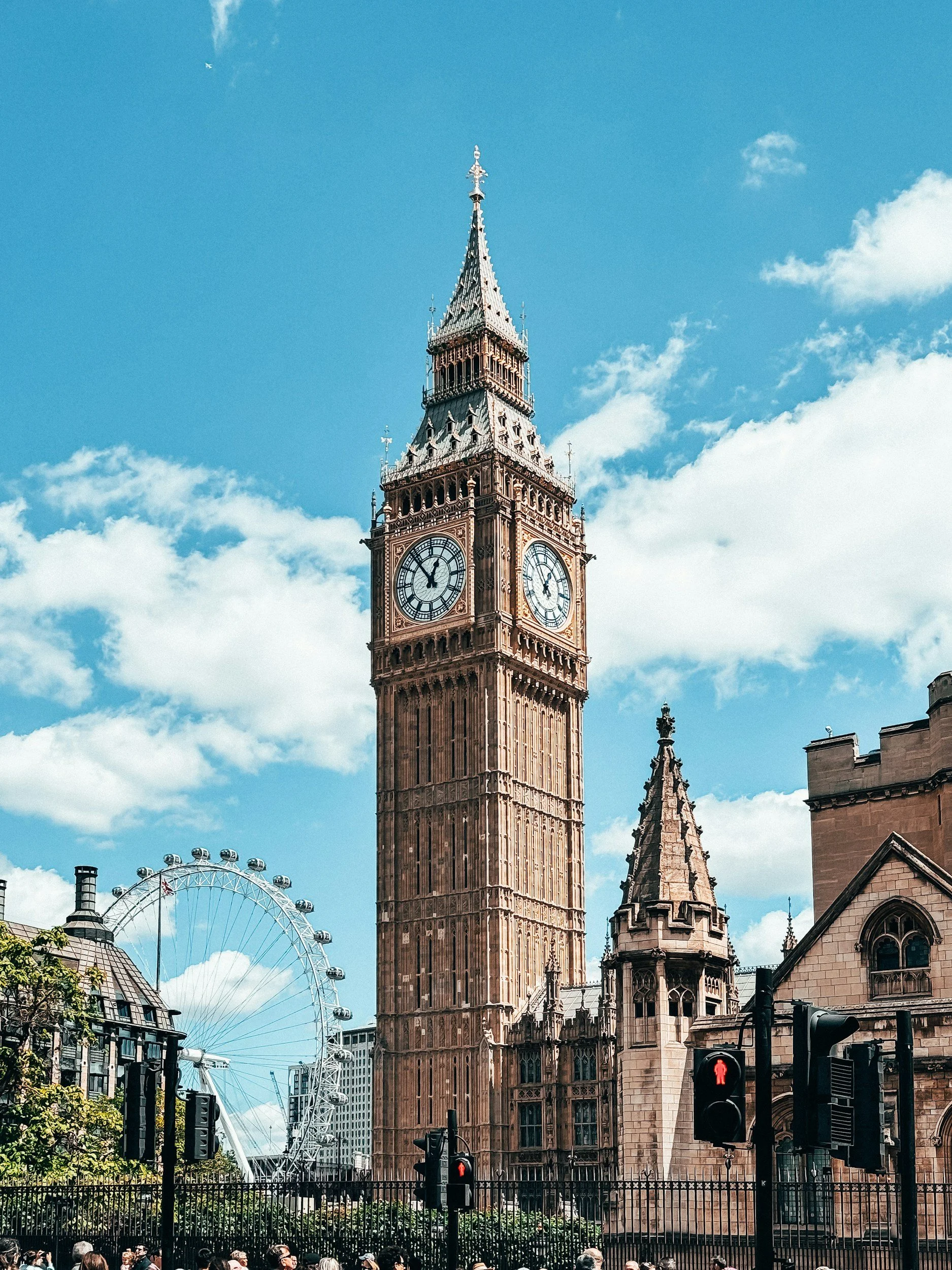 La torre del reloj Big Ben en Londres, con una noria en el fondo y semáforos en primer plano.