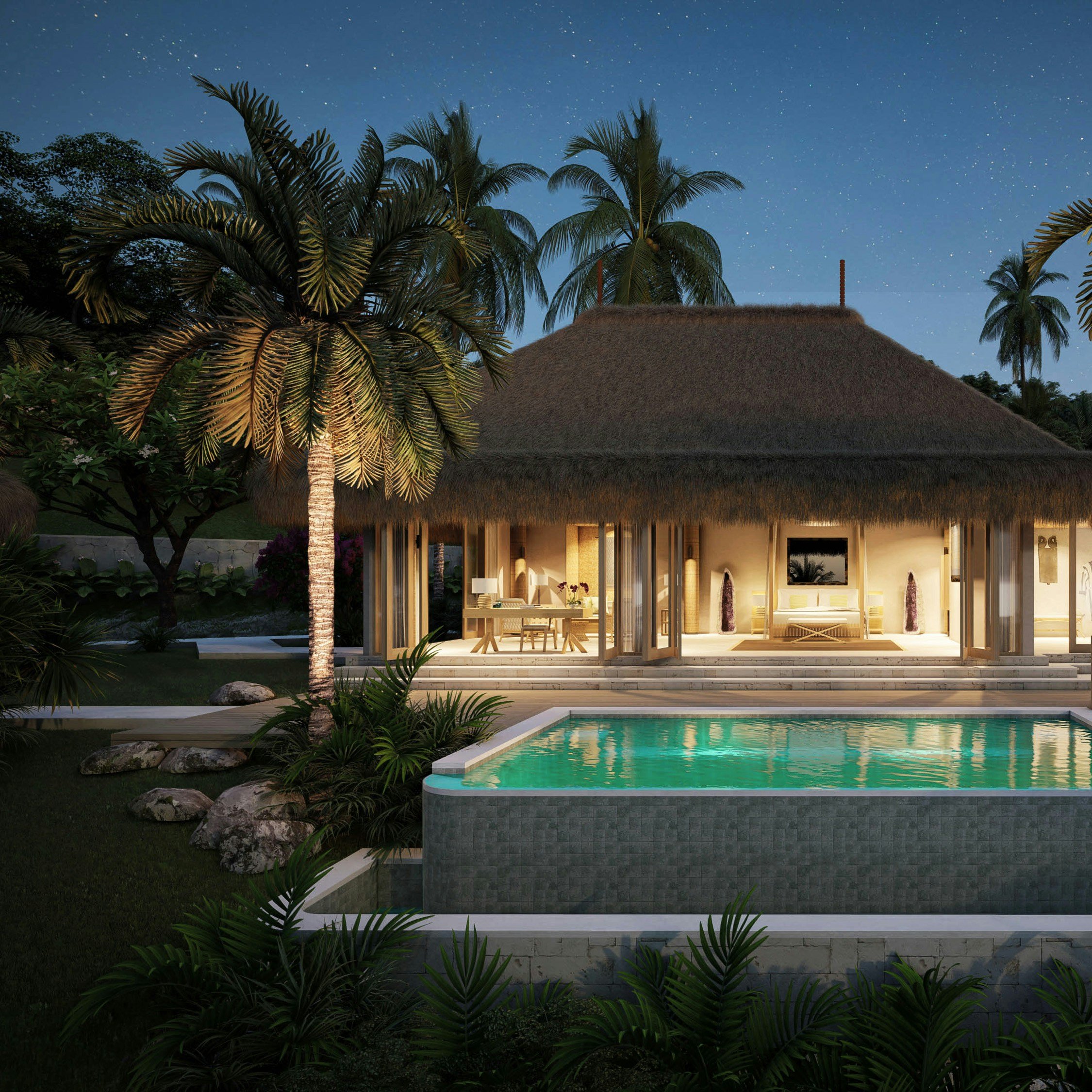 Casa de playa con techo de paja, luces en el interior, piscina al frente y palmeras, al anochecer.