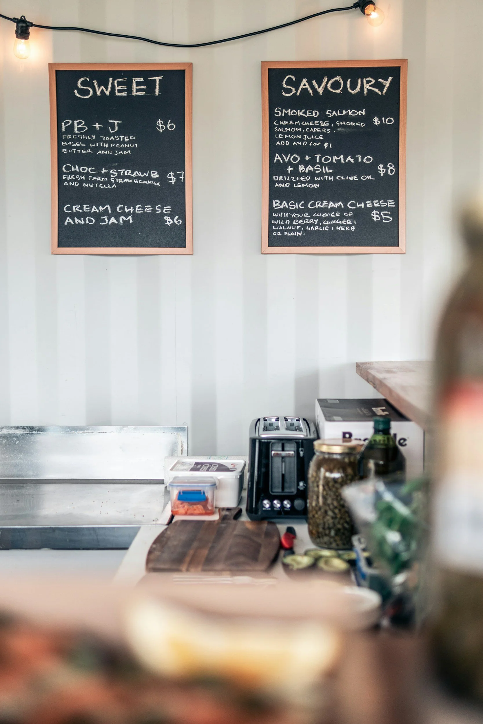 Carteles en la pared con menús de comida en un restaurante o cafetería, y una mesa con utensilios y alimentos en primer plano.