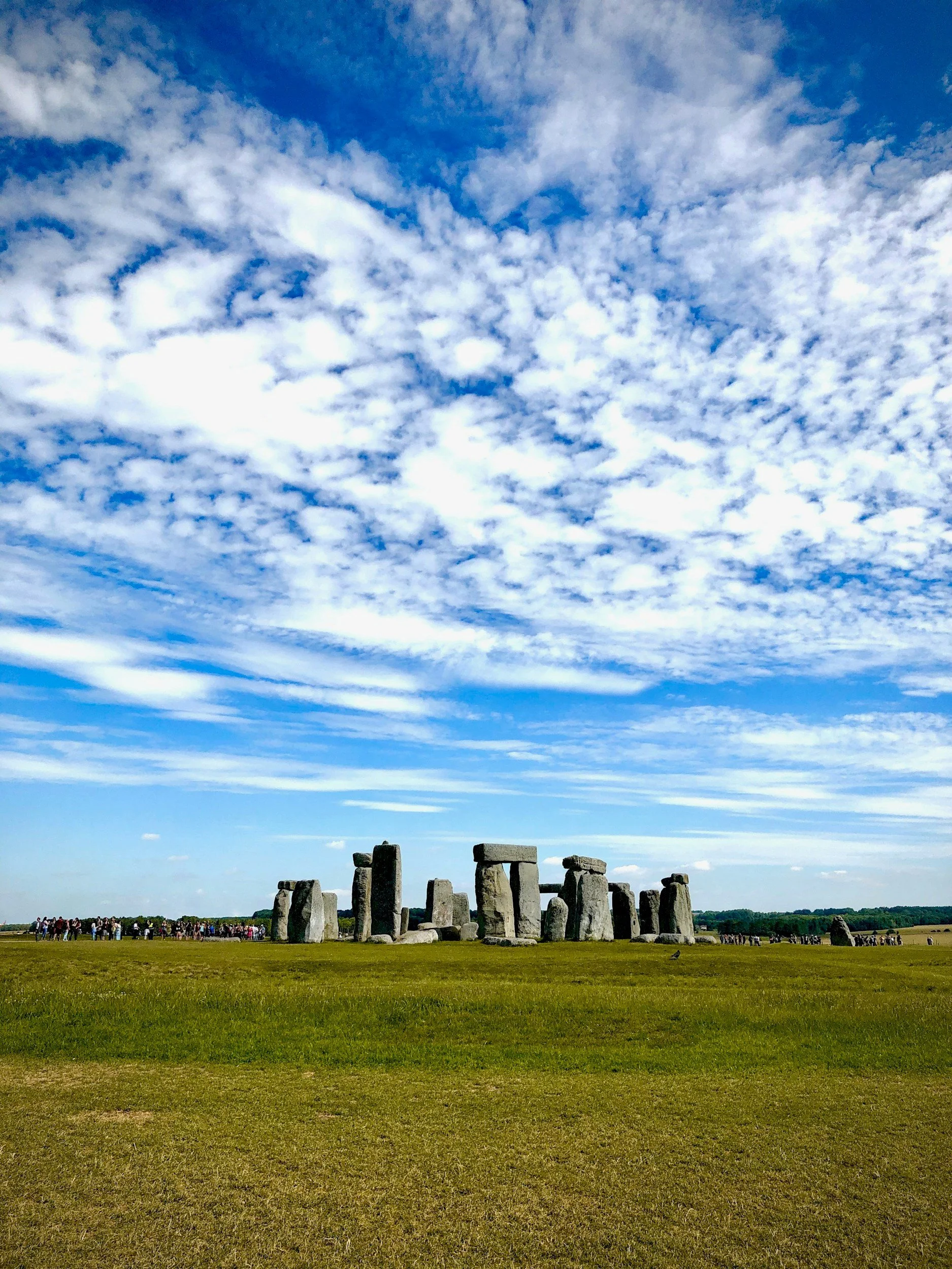 Vista del monumento de Stonehenge en un día soleado, con muchas personas al fondo y un cielo con nubes dispersas.