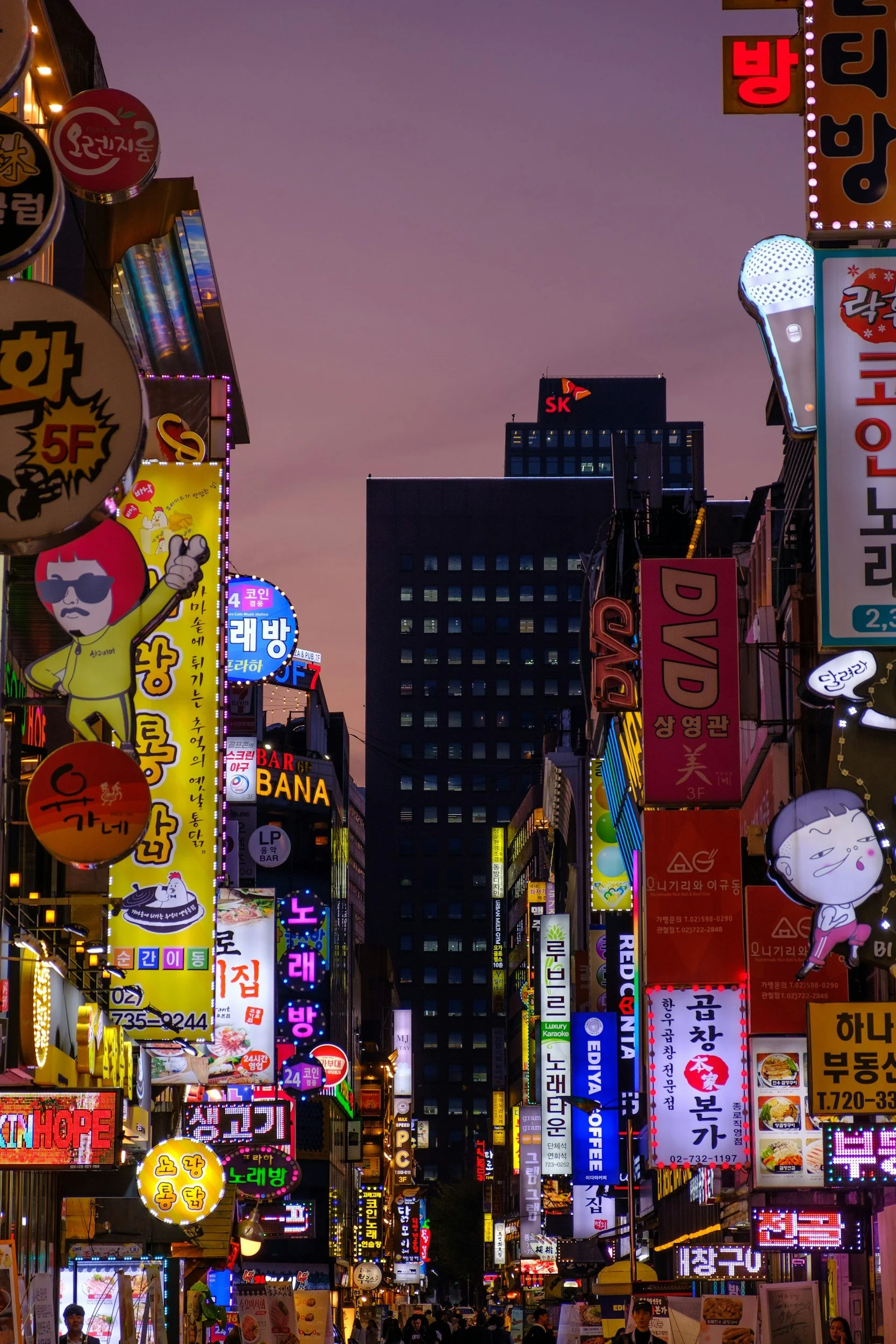 Vista de una calle llena de letreros luminosos en coreano en una ciudad durante la noche.