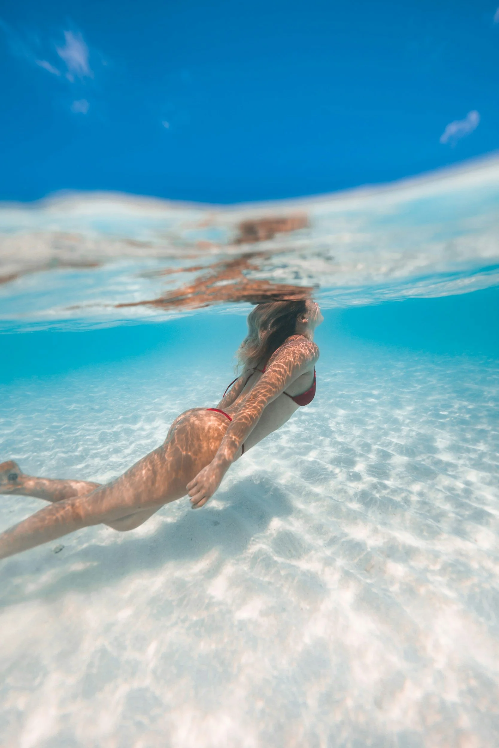 Mujer en bikini nadando en el océano, vista parcialmente sumergida, con cielo azul y agua clara alrededor.