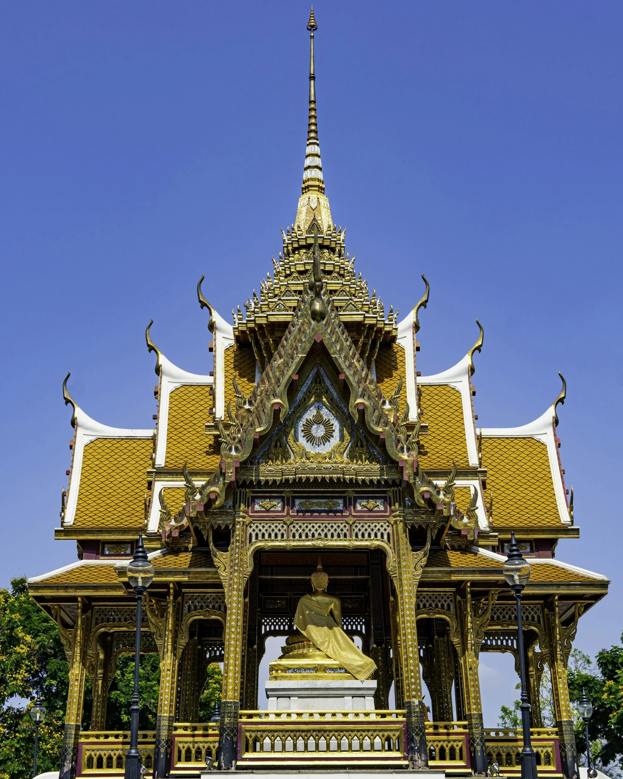 Templo tailandés dorado con techo naranja y estructura ornamentada, con estatua dorada en el interior y farolas en el exterior, bajo cielo azul.