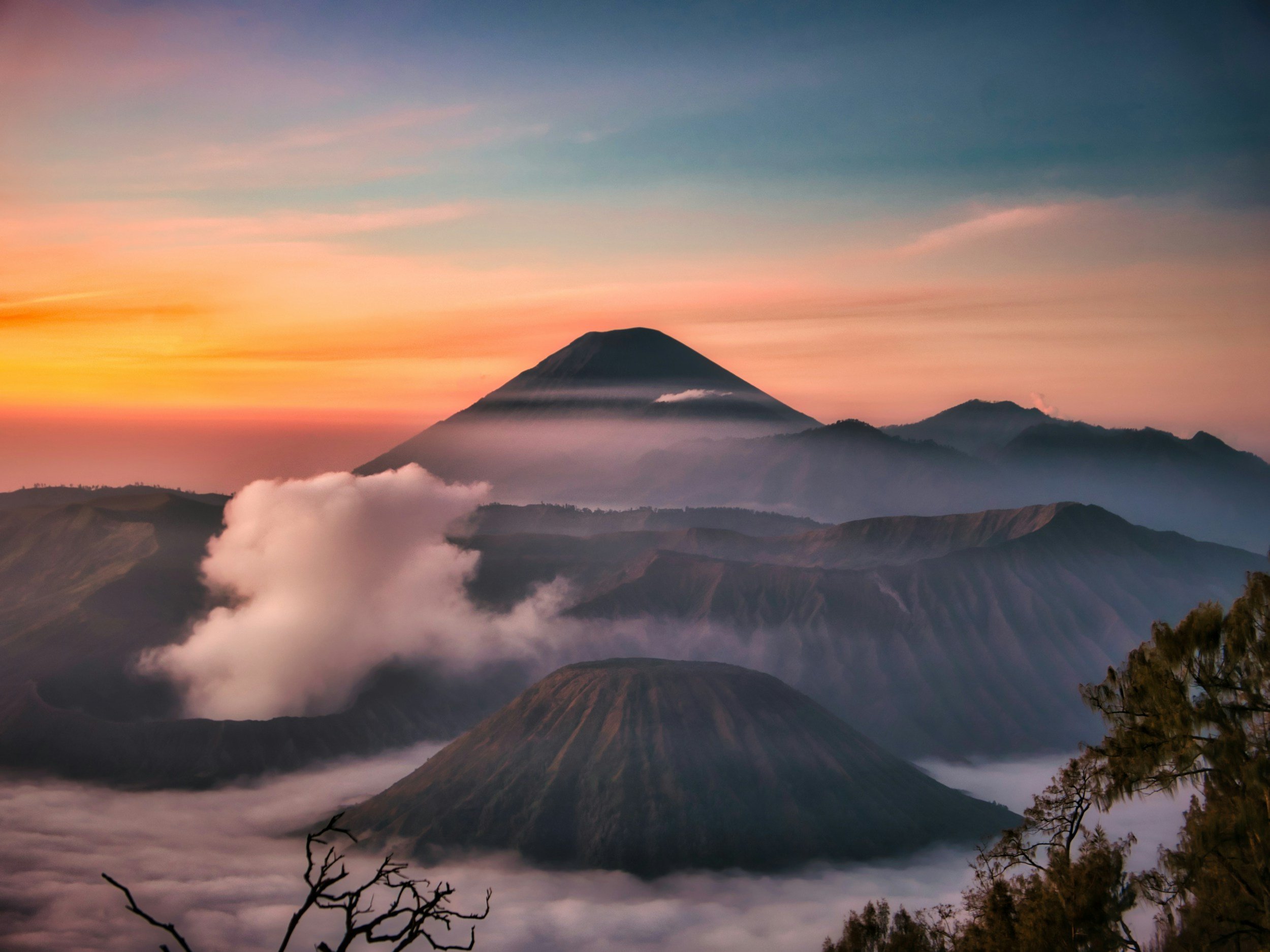 Paisaje de volcanes con nubes y cielo al amanecer o atardecer, en tonos cálidos y fríos.