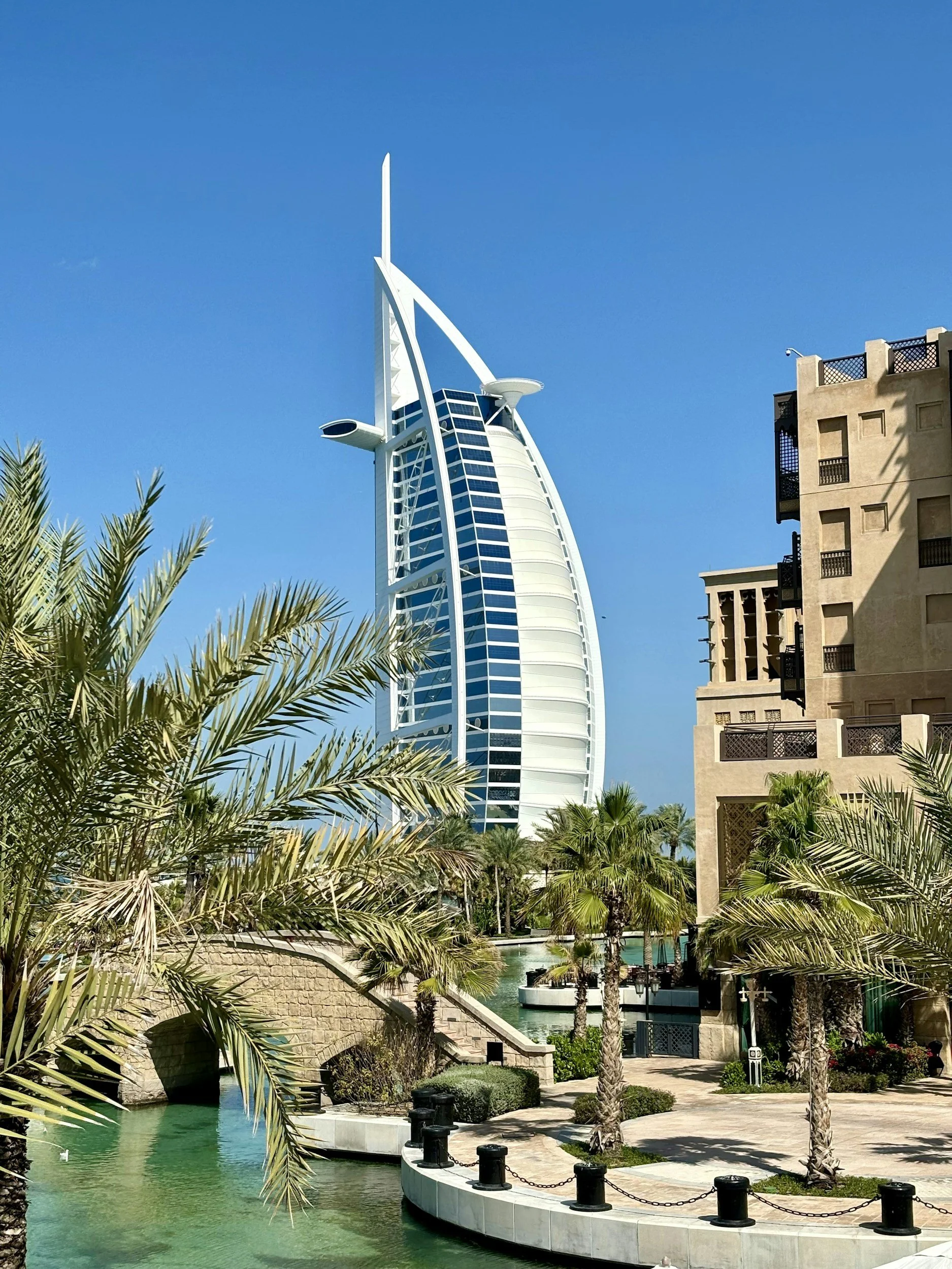 El hotel Burj Al Arab en Dubái con un diseño en forma de vela, rodeado de palmeras y jardines acuáticos bajo un cielo azul