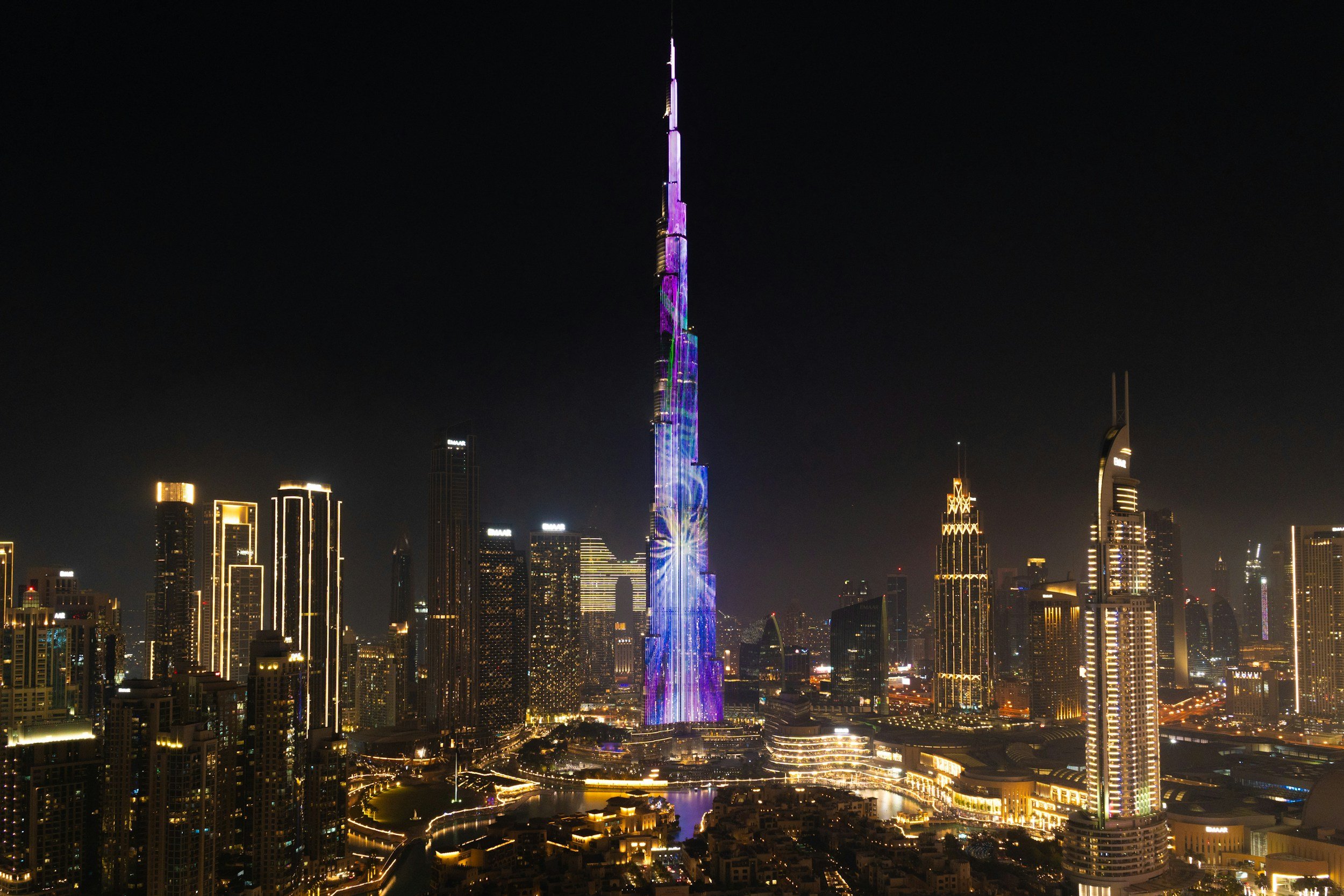 Vista nocturna del skyline de Dubái con el Burj Khalifa iluminado con colores morados y azules.
