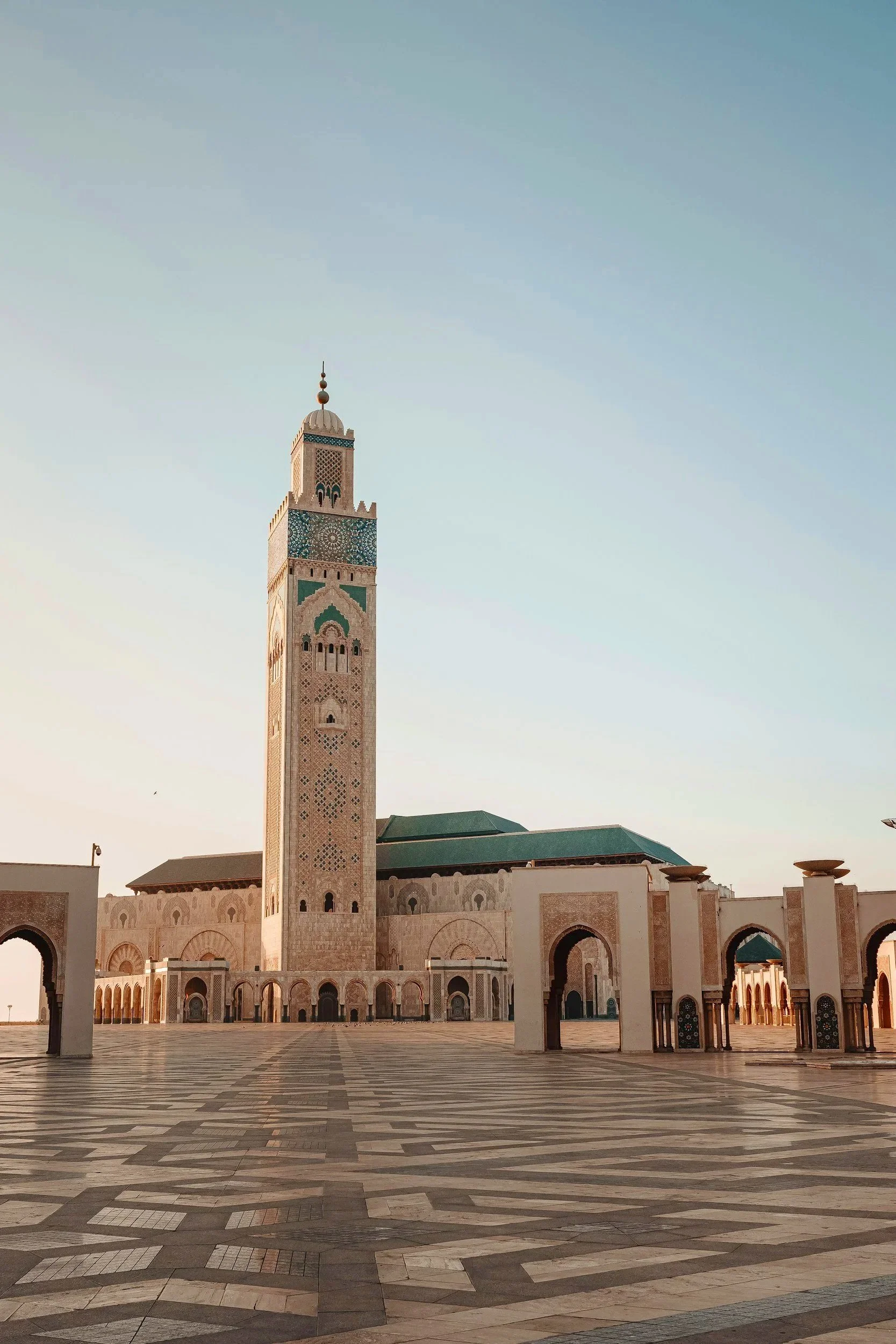 Una mezquita con una torre alta y detalles en azul y beige, en un espacio abierto con piso de mosaico en patrones geométricos.