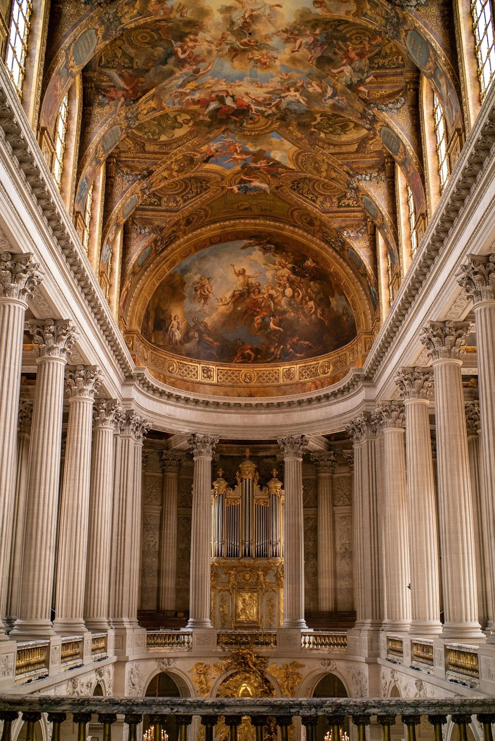 Interior de una iglesia o catedral con columnas de mármol, un gigantesco órgano y un techo decorado con frescos y dorados.