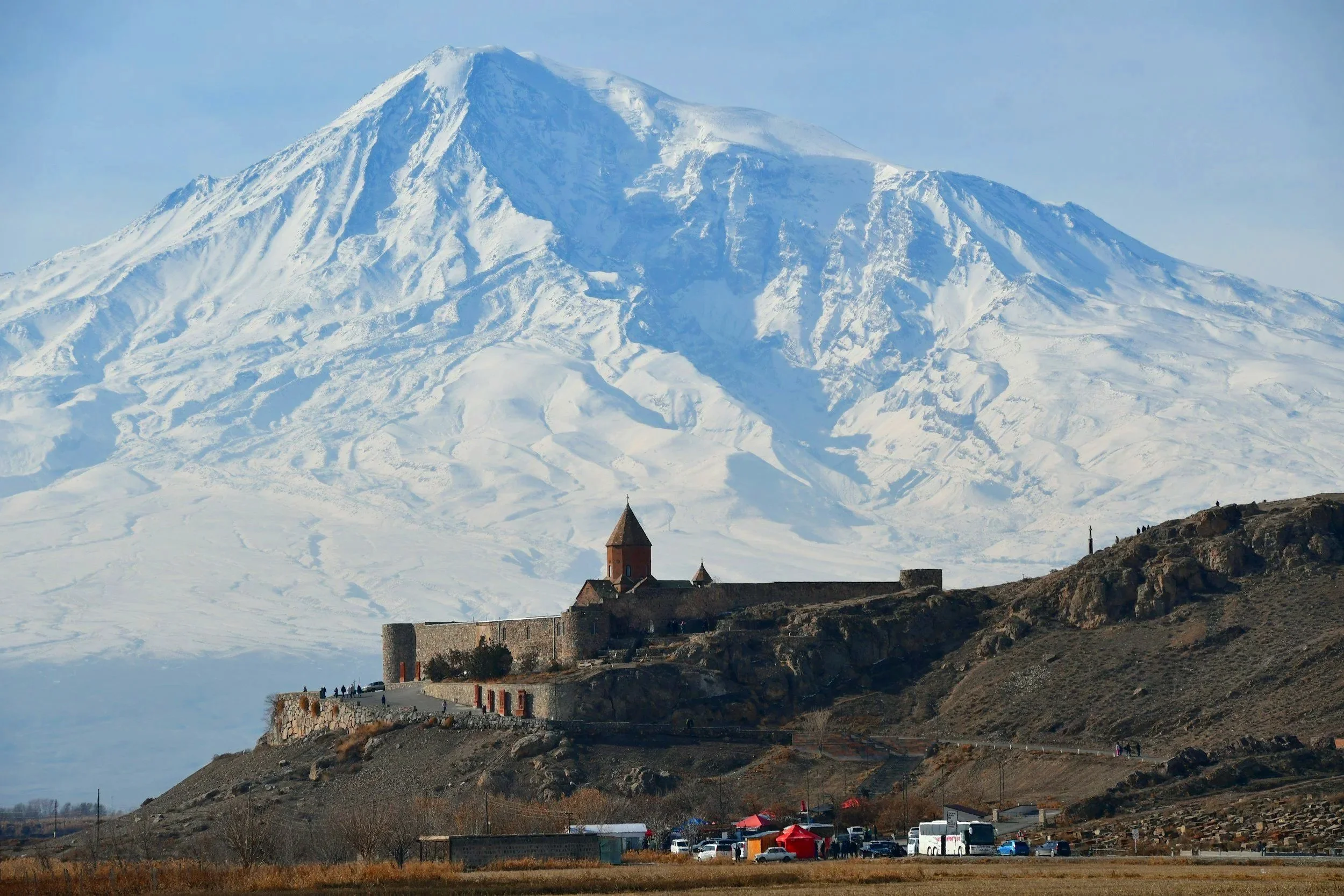 Vista de un volcán cubierto de nieve con una iglesia y un muro de piedra en primer plano, en un paisaje montañoso.