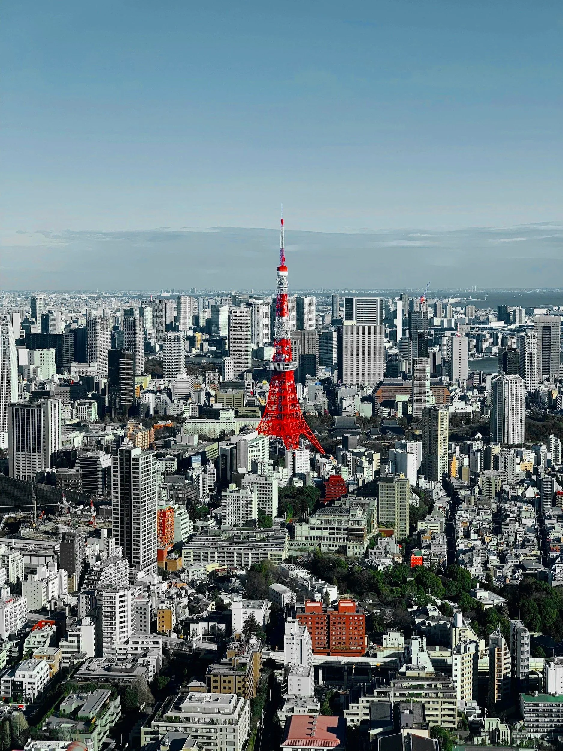 Vista aérea de la ciudad de Tokio con la Torre de Tokio en primer plano, rodeada de muchos edificios y rascacielos, con un cielo parcialmente nublado.