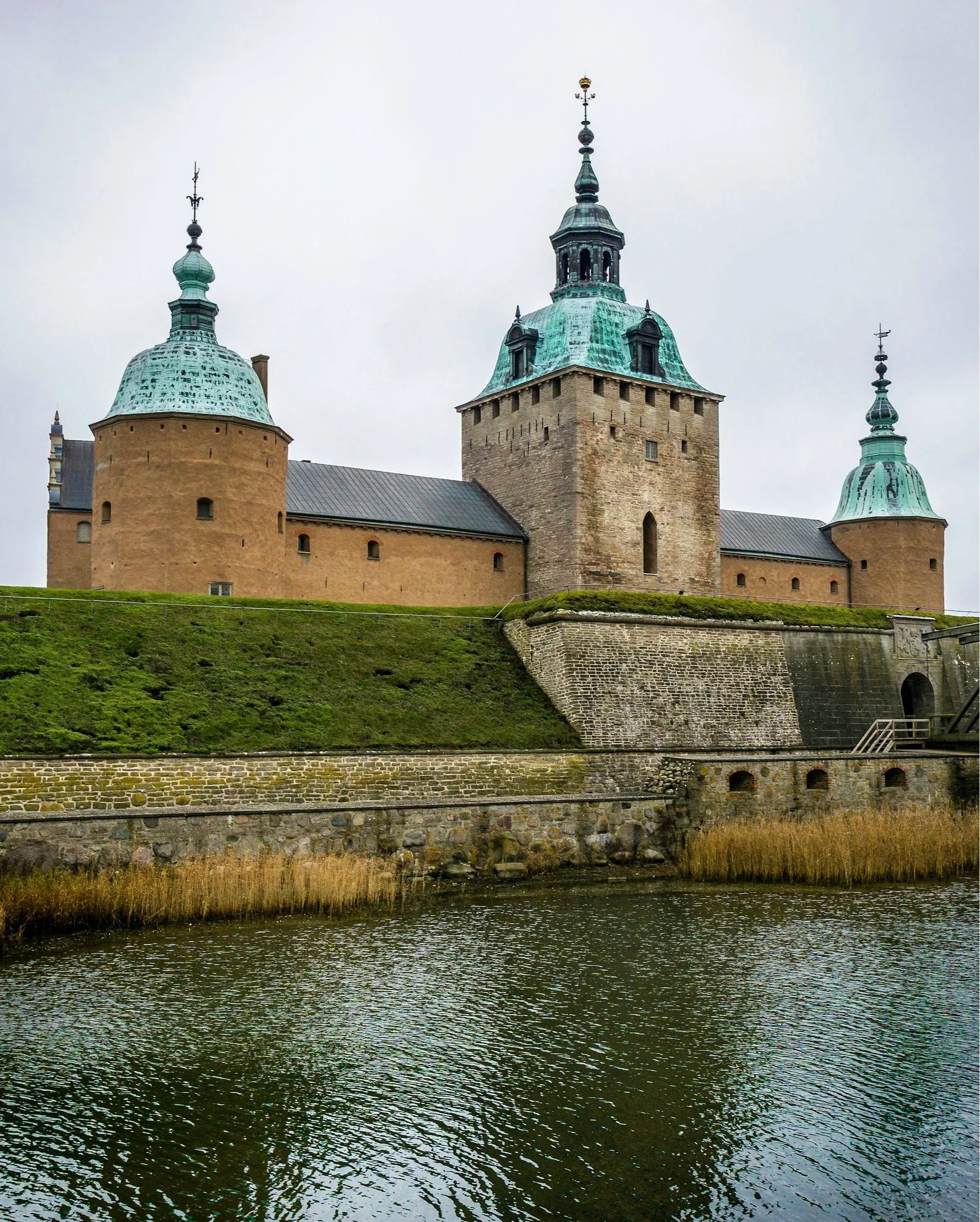 Castillo medieval en un entorno junto a un río, con torres y murallas de piedra y techo de cobre