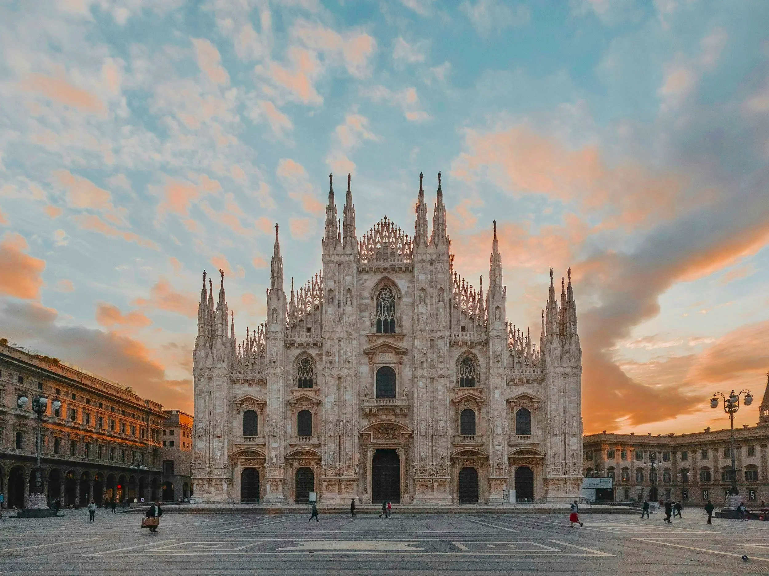 Vista del Duomo de Milán al atardecer con cielo nublado y personas caminando en la plaza.